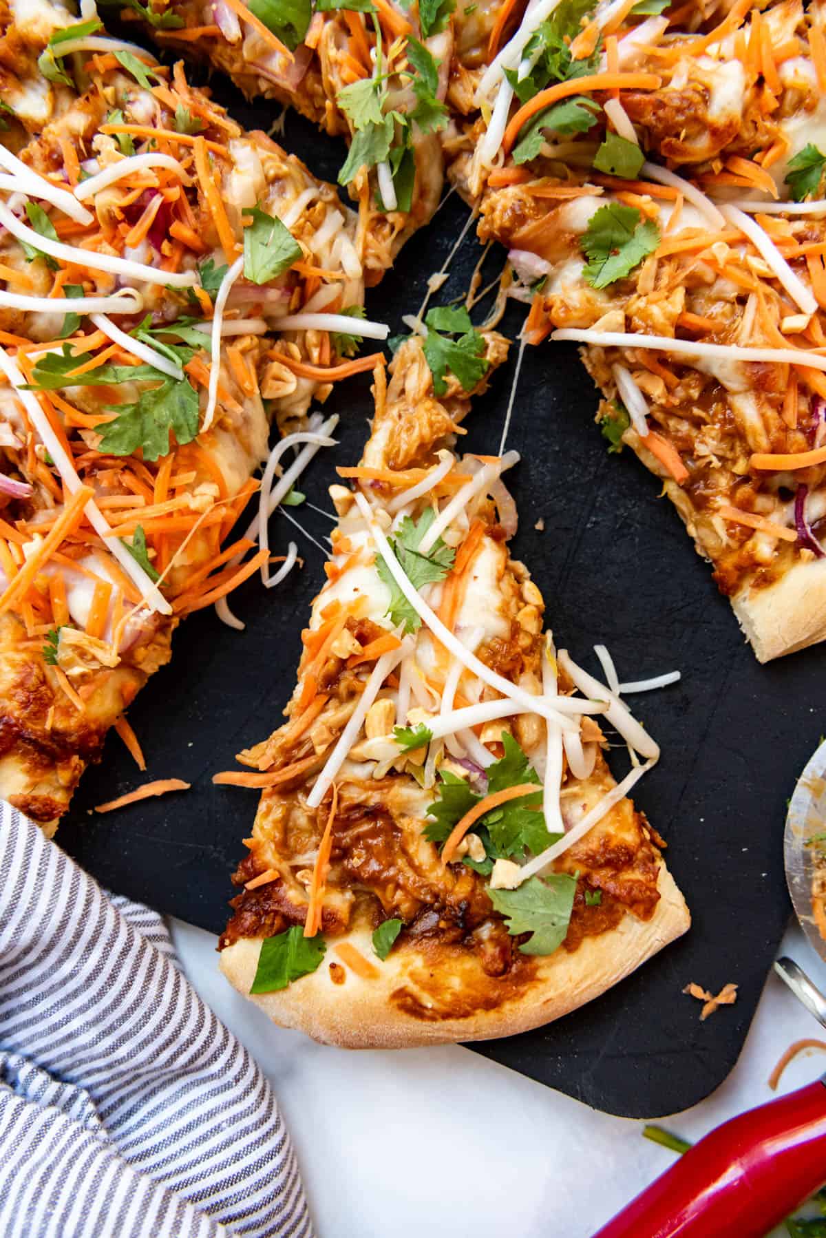 A slice of Thai chicken pizza on a black cutting board.