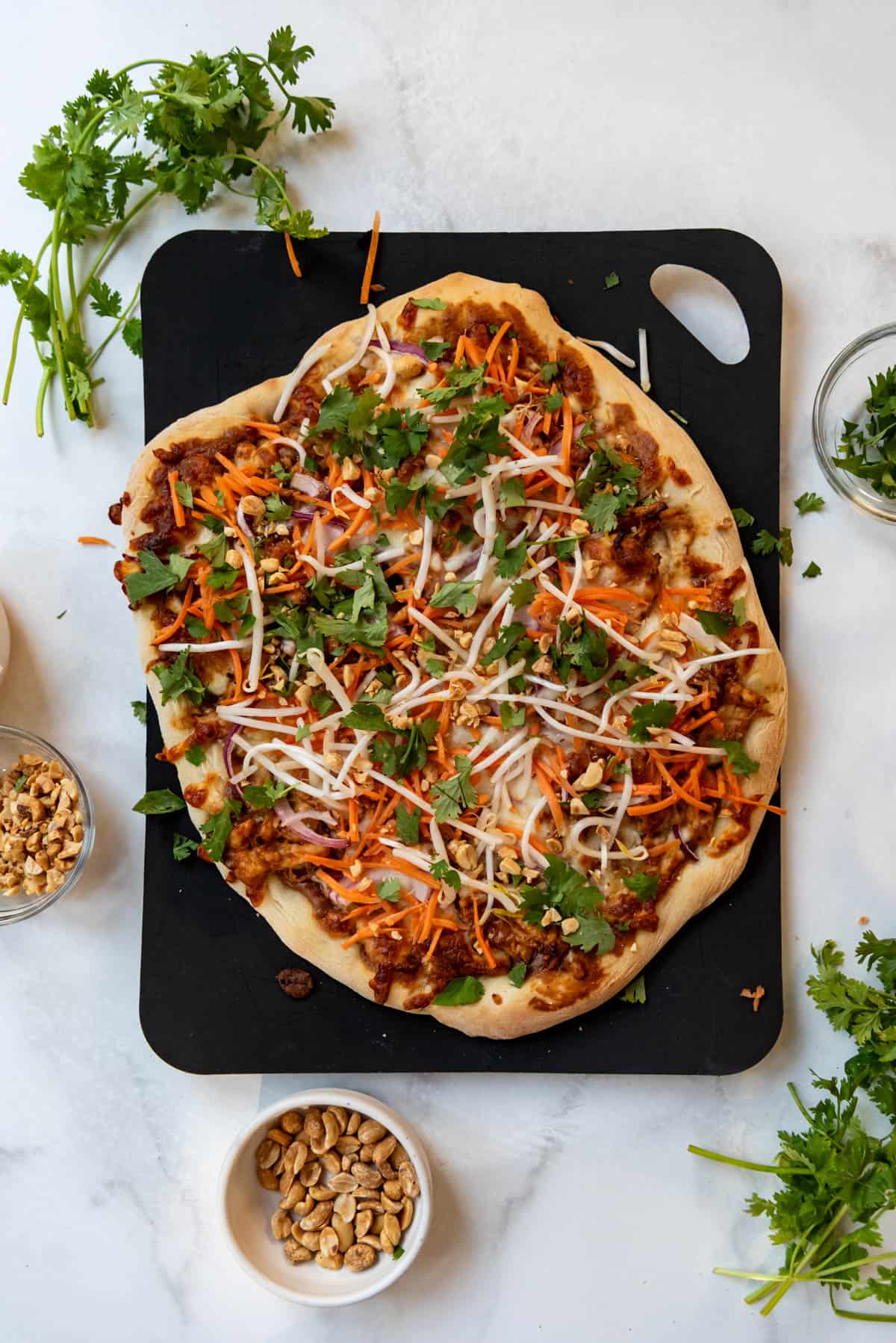 A finished Thai chicken pizza topped with shredded carrots, cilantro, and bean sprouts.