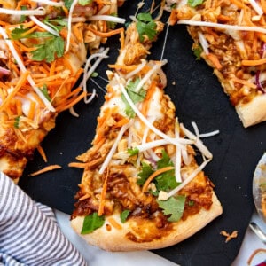 A slice of Thai chicken pizza on a black cutting board.