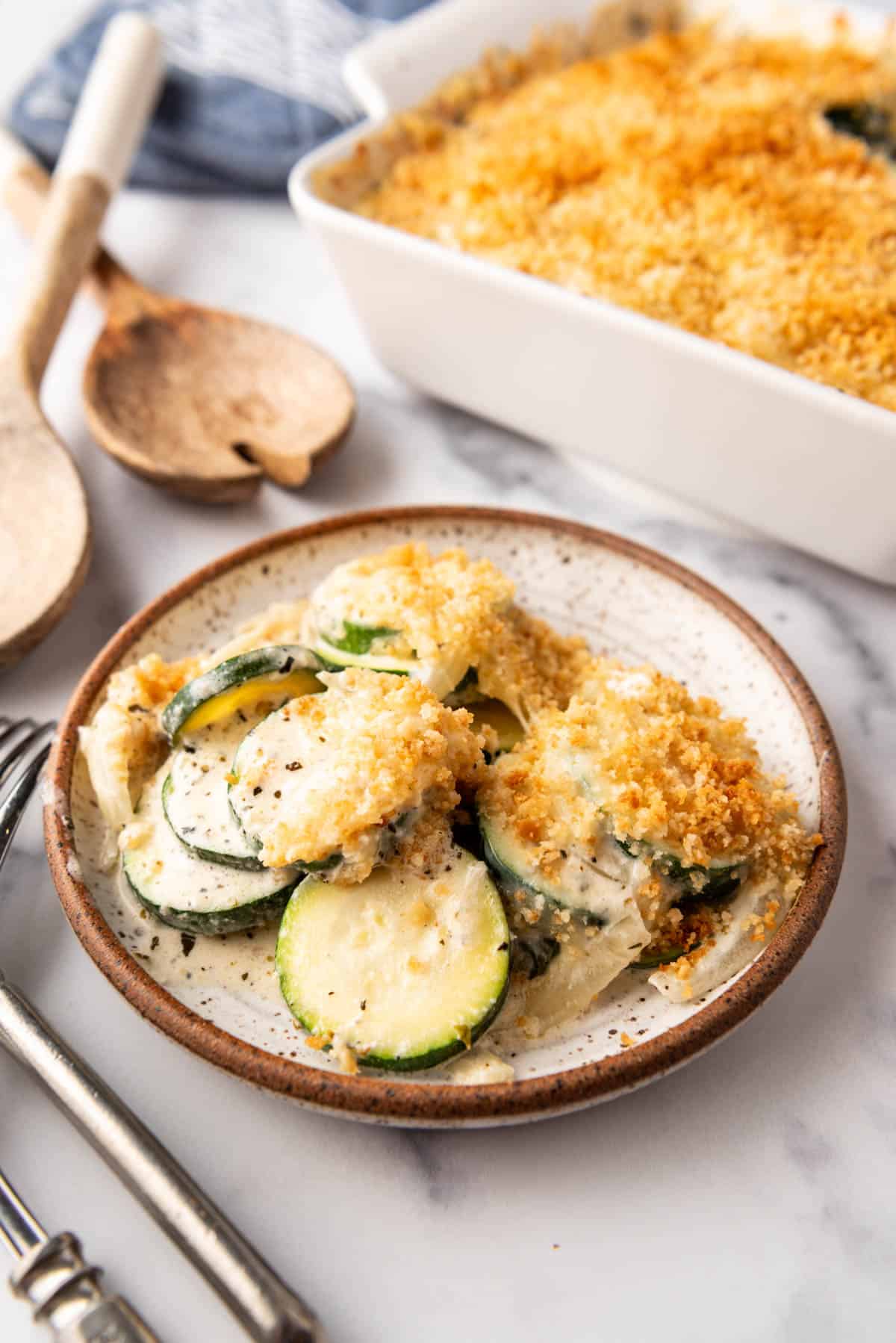 A plate of zucchini casserole in front of a white baking dish.