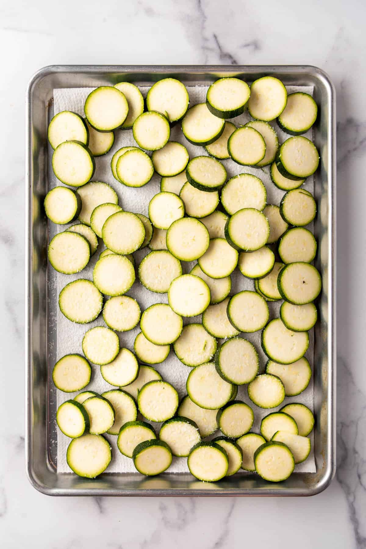 Sliced zucchini sprinkled with salt on a baking sheet.