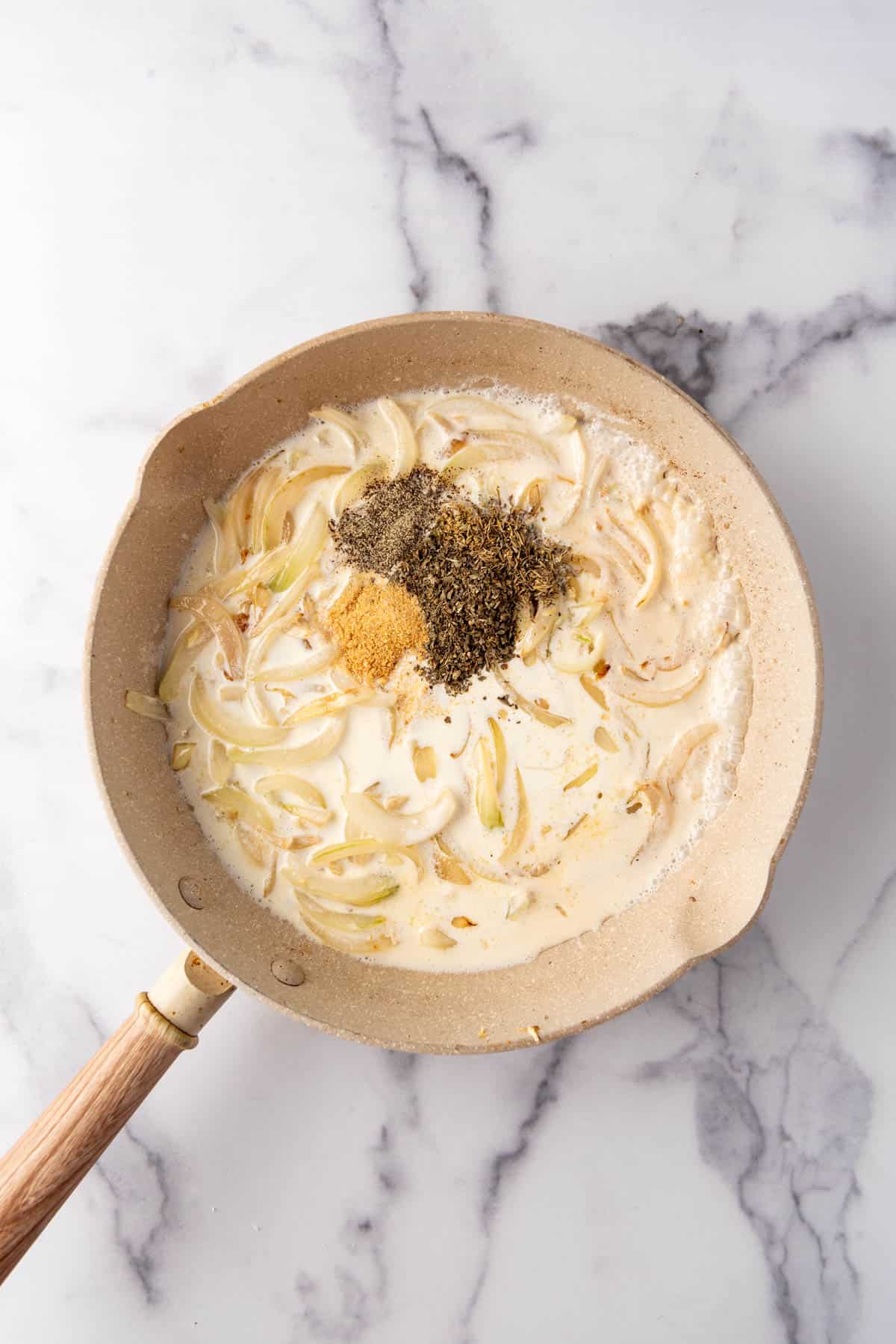 Adding cream, spices, and herbs to sauteed onions and garlic in a pan.