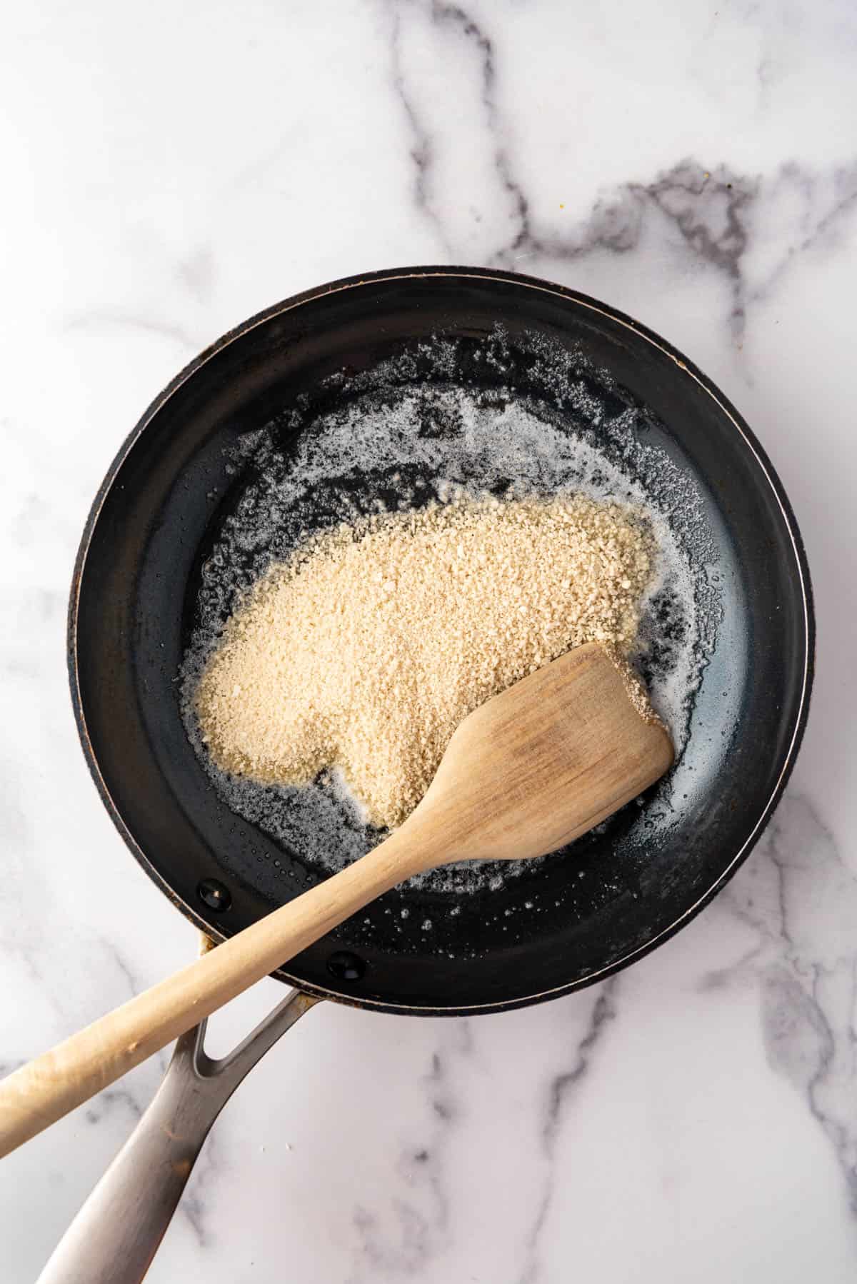 Toasting Panko breadcrumbs in butter in a pan with a wooden spoon.