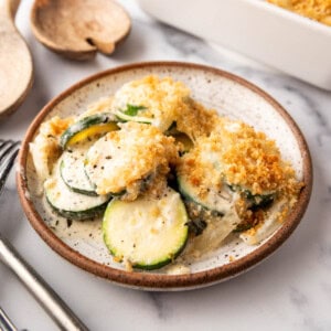 A plate of zucchini casserole in front of a white baking dish.