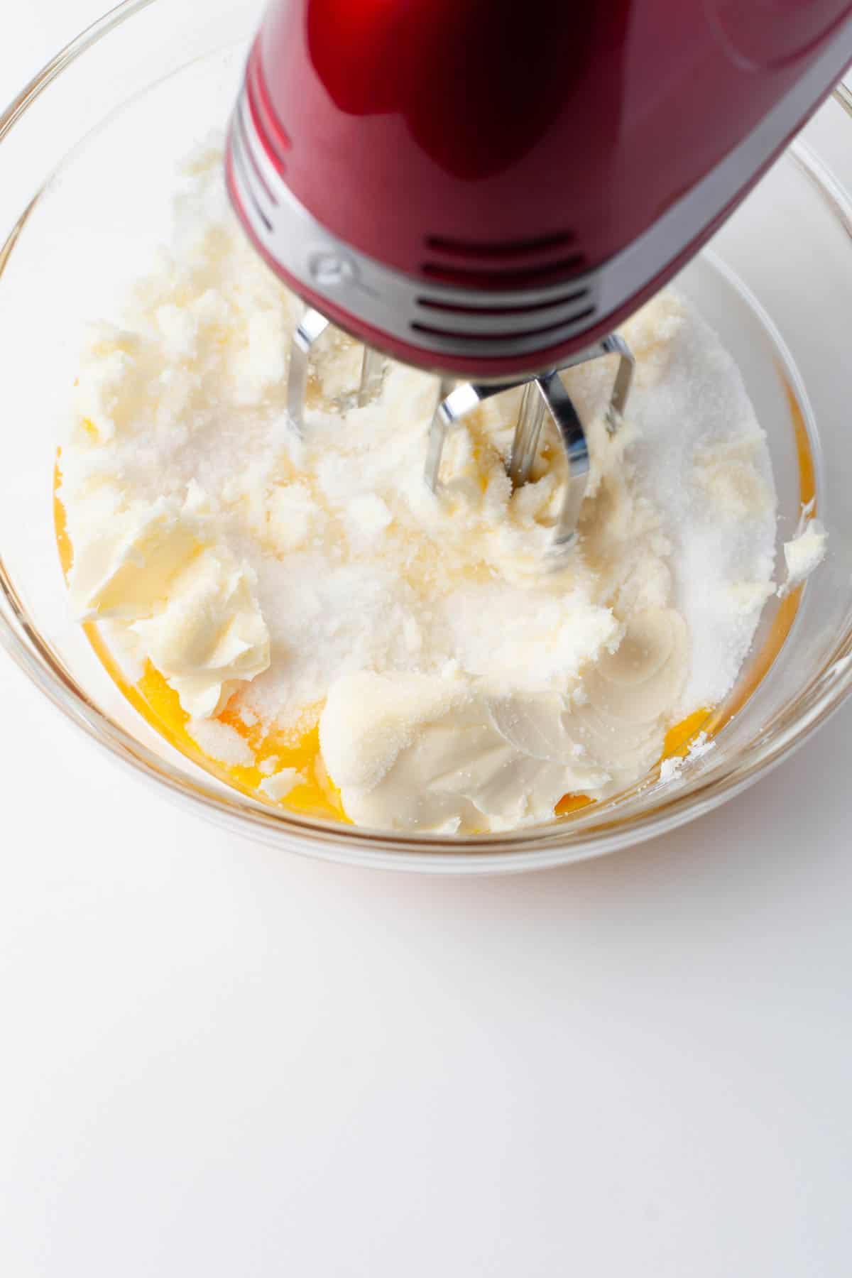 Close up view of granulated sugar, egg yolks, and butter being mixed together in a glass mixing bowl.