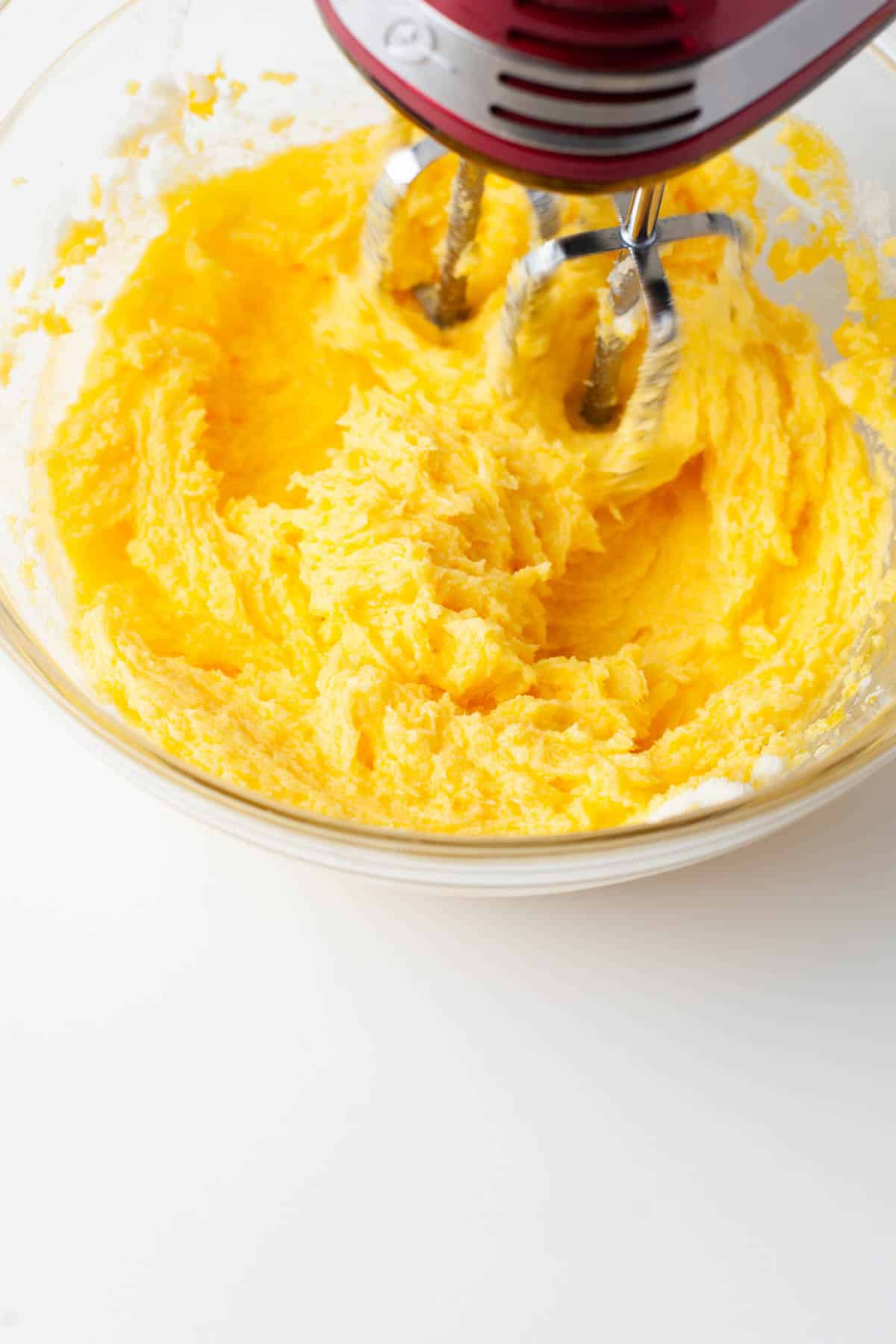 Close up view of granulated sugar, egg yolks, and butter mixed together in a glass mixing bowl.