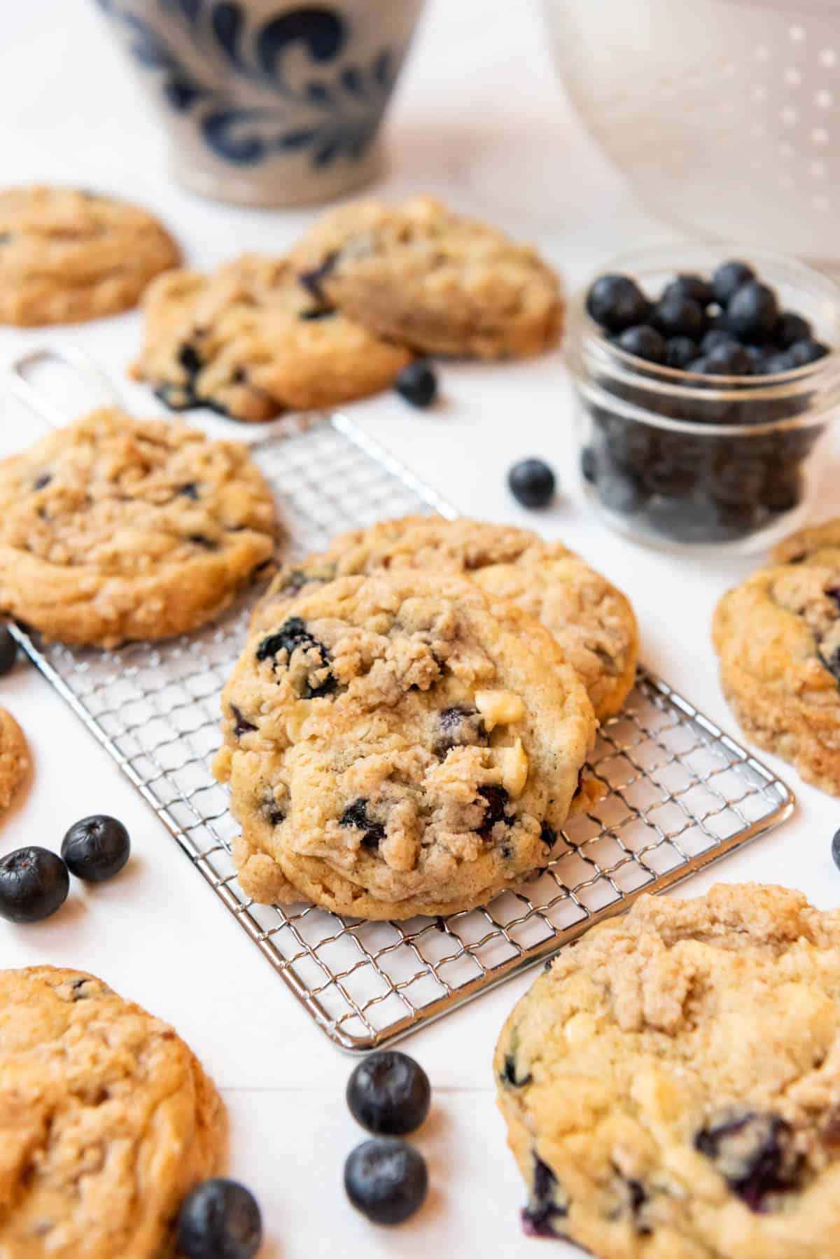 An image of blueberry muffin cookies on a wire rack with fresh blueberries nearby.