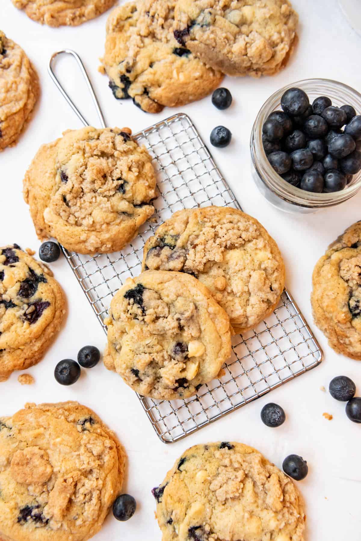 Blueberry muffin cookies on a small wire rack with a bowl of blueberries nearby.