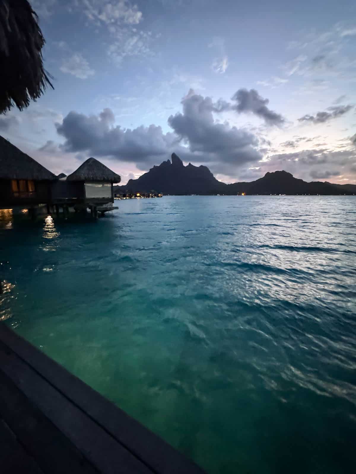 An image of sunset over Bora Bora with an over-the-water bungalow in the foreground.