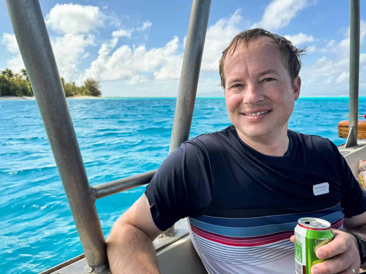 An image of a man in a rash guard holding a can of juice on a boat in Bora Bora.