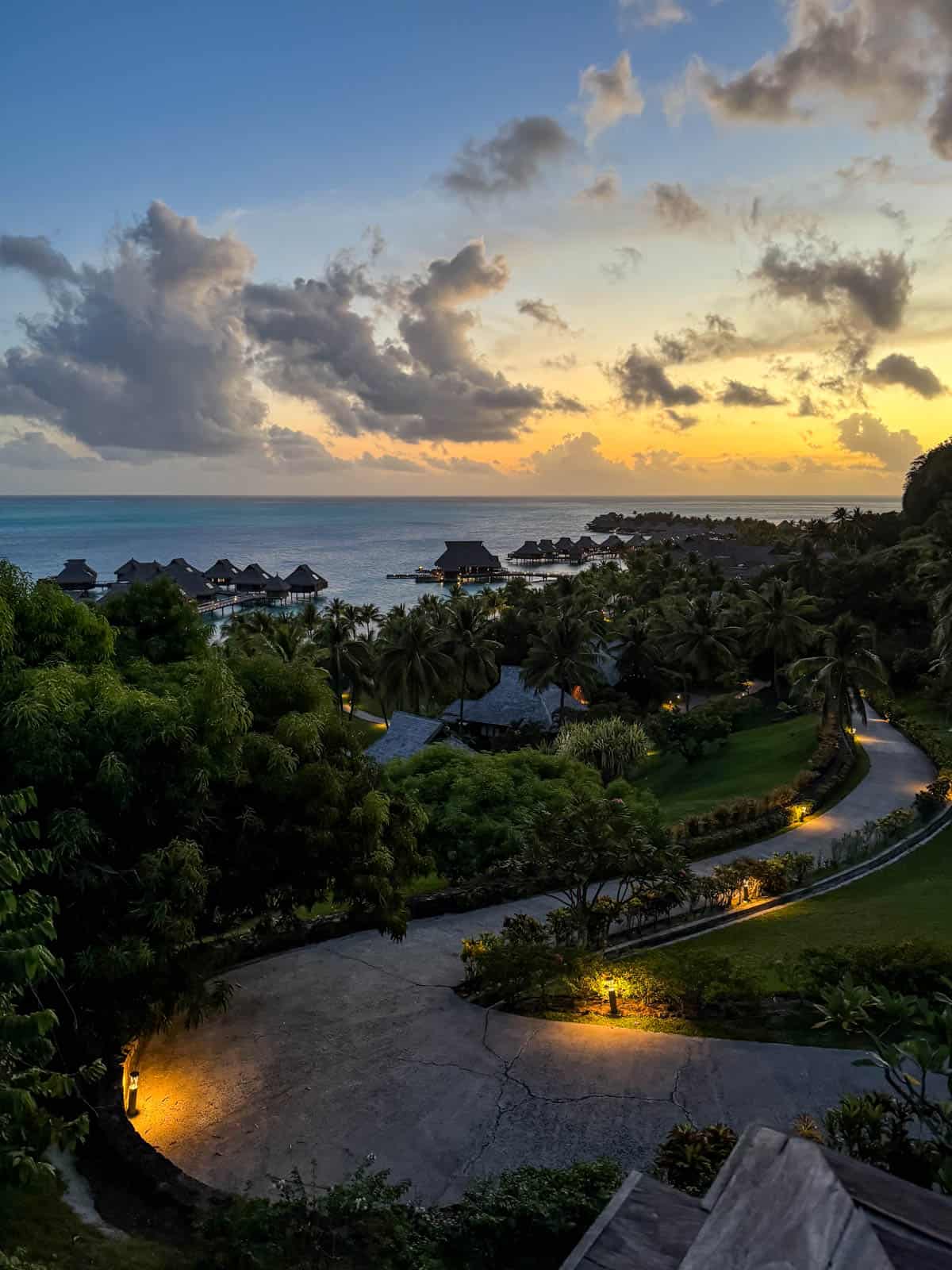 An image of a lit path from the top of a hill overlooking the ocean at dusk in Bora Bora.