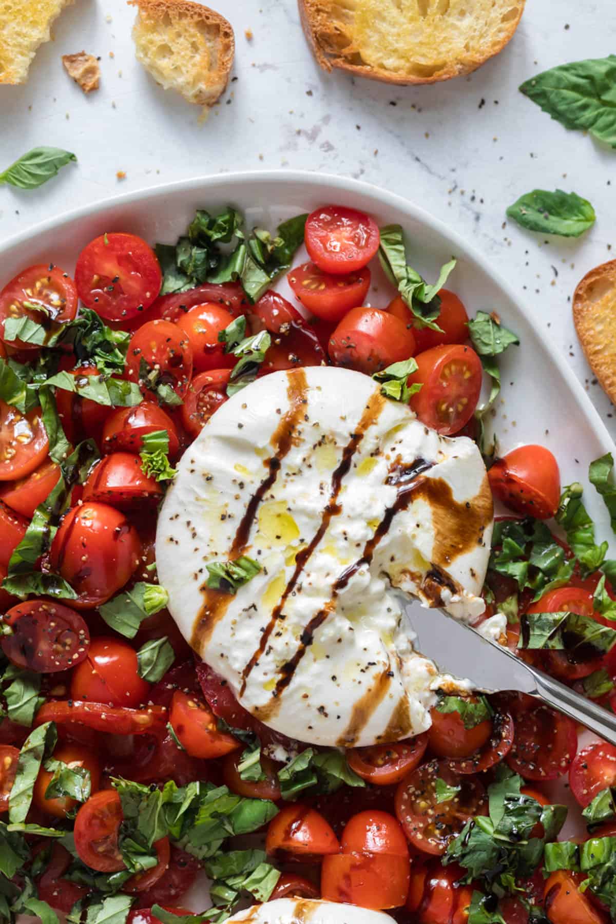 A close image of a ball of burrata cheese on top of tomatoes and basil leaves.