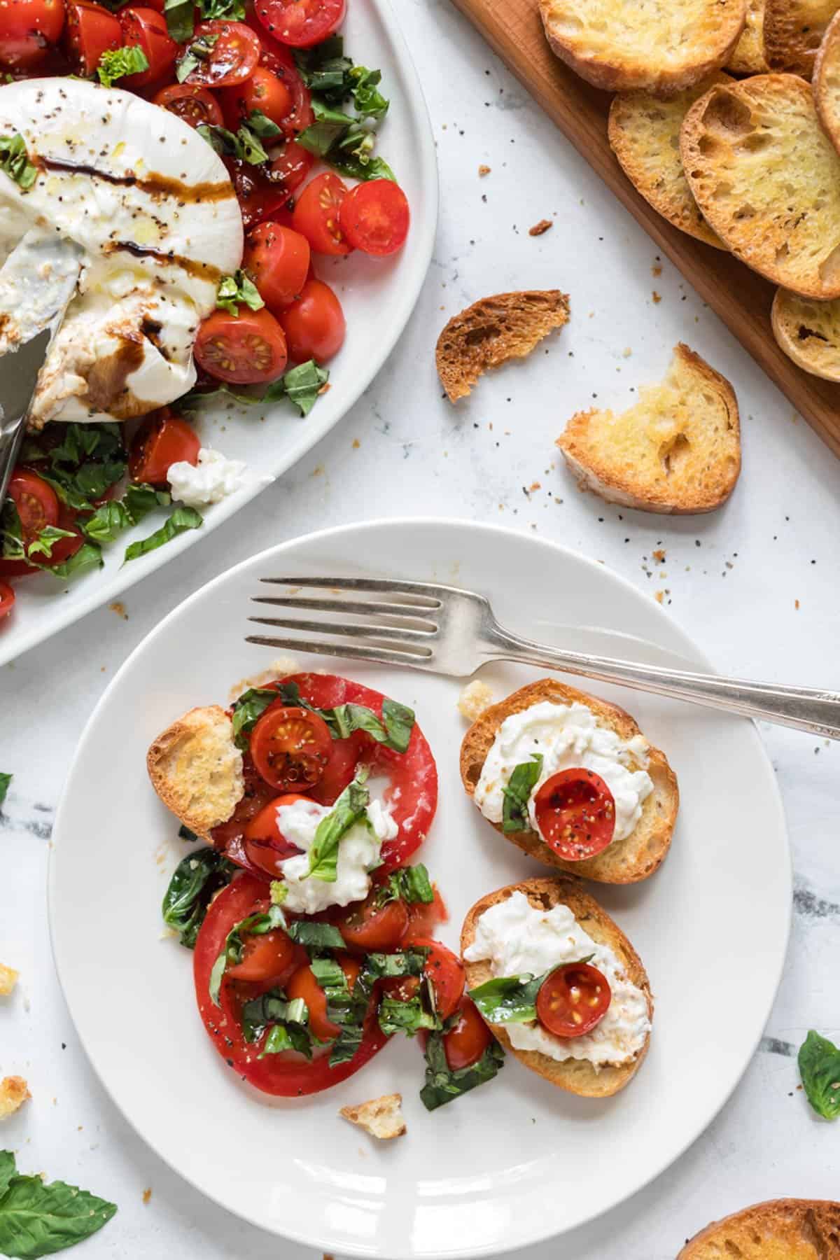 An overhead image of a plate of burrata caprese with toasted baguette and a fork.