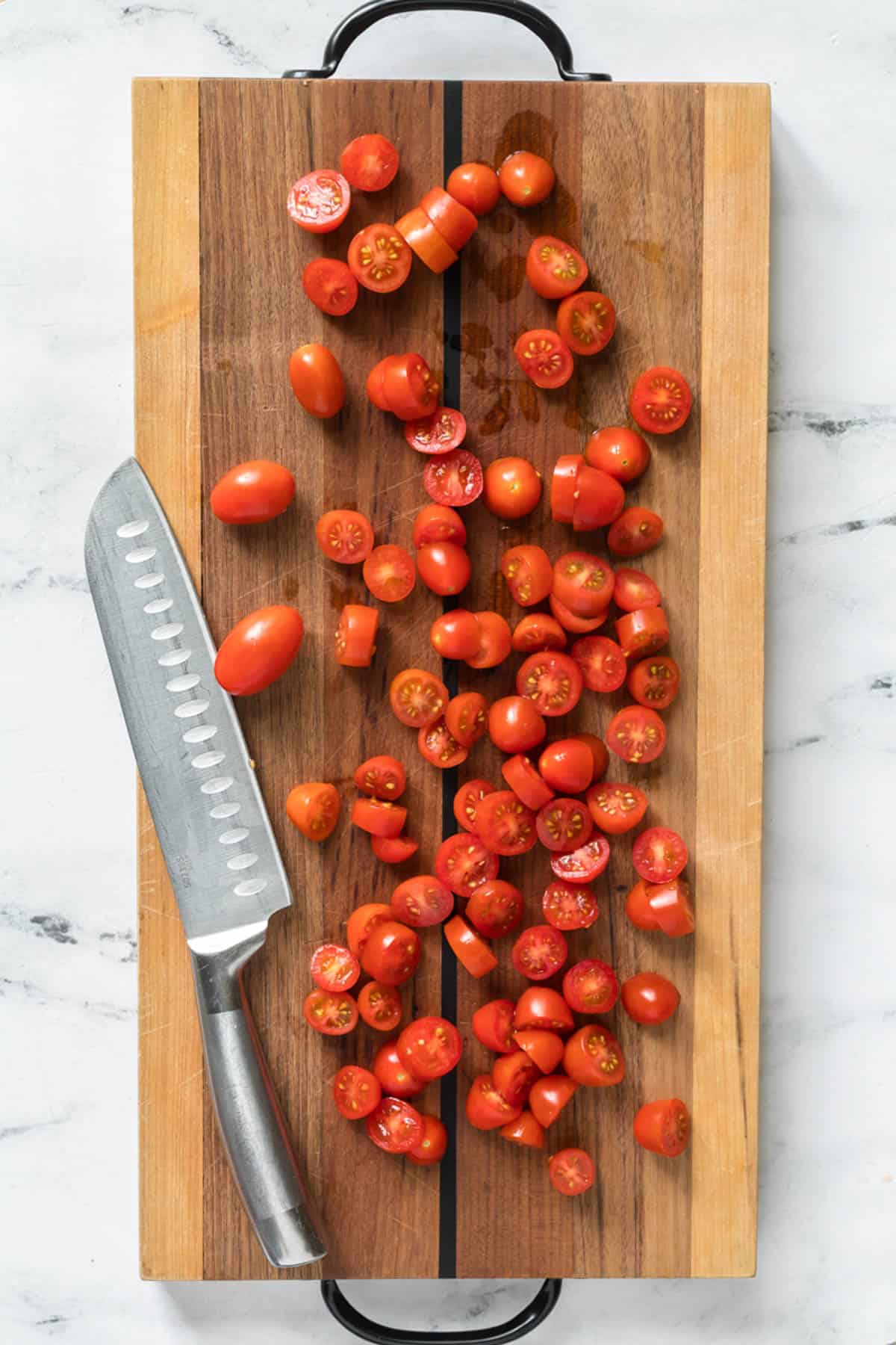 Sliced cherry tomatoes on a cutting board with a knife.