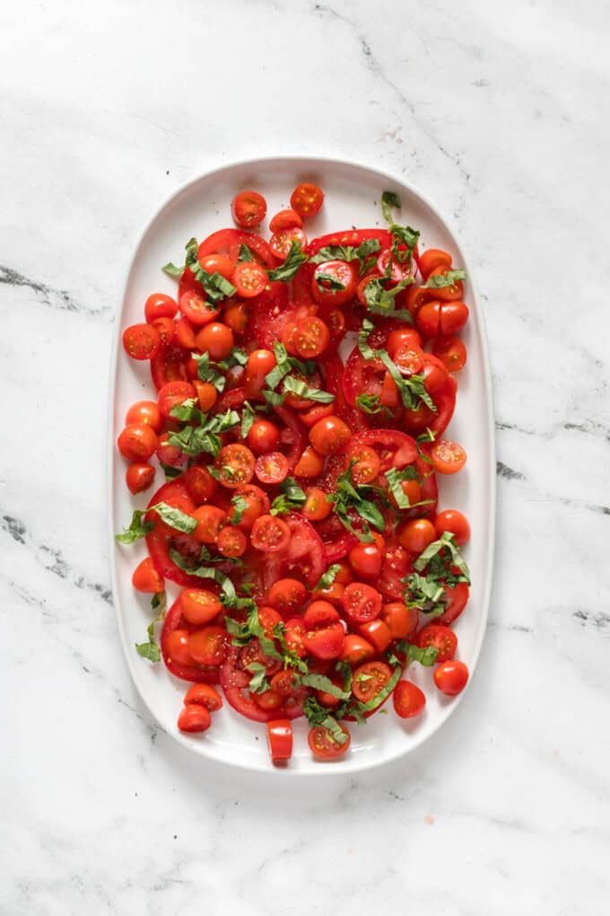 Adding chopped basil to a plate of tomatoes.