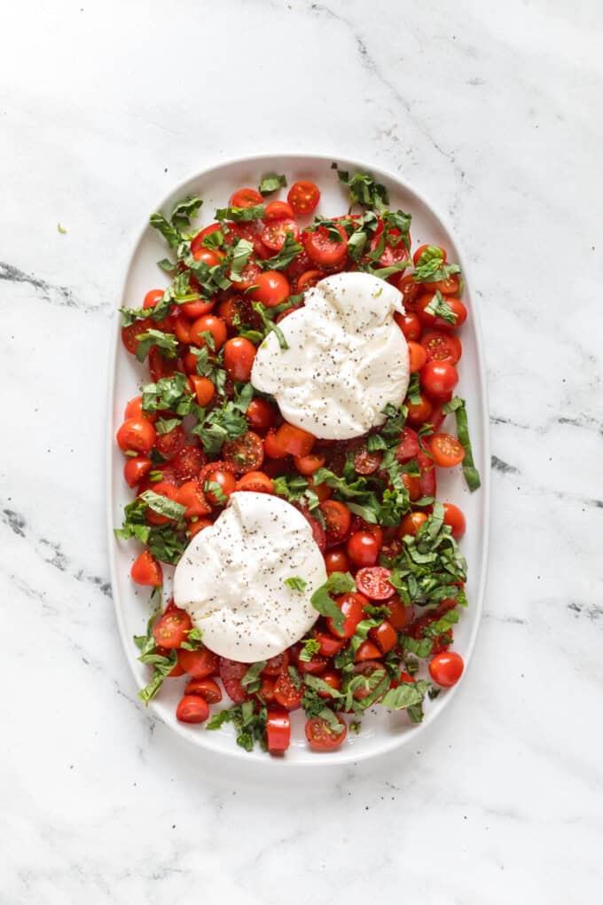 Balls of burrata cheese that have been sliced open to show the creamy centers on top of tomatoes and basil.