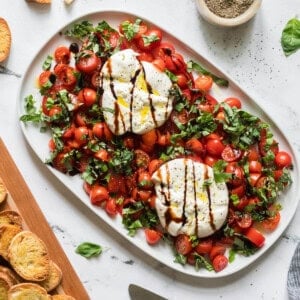 An overhead image of a platter of burrata caprese with toasted bread next to it.