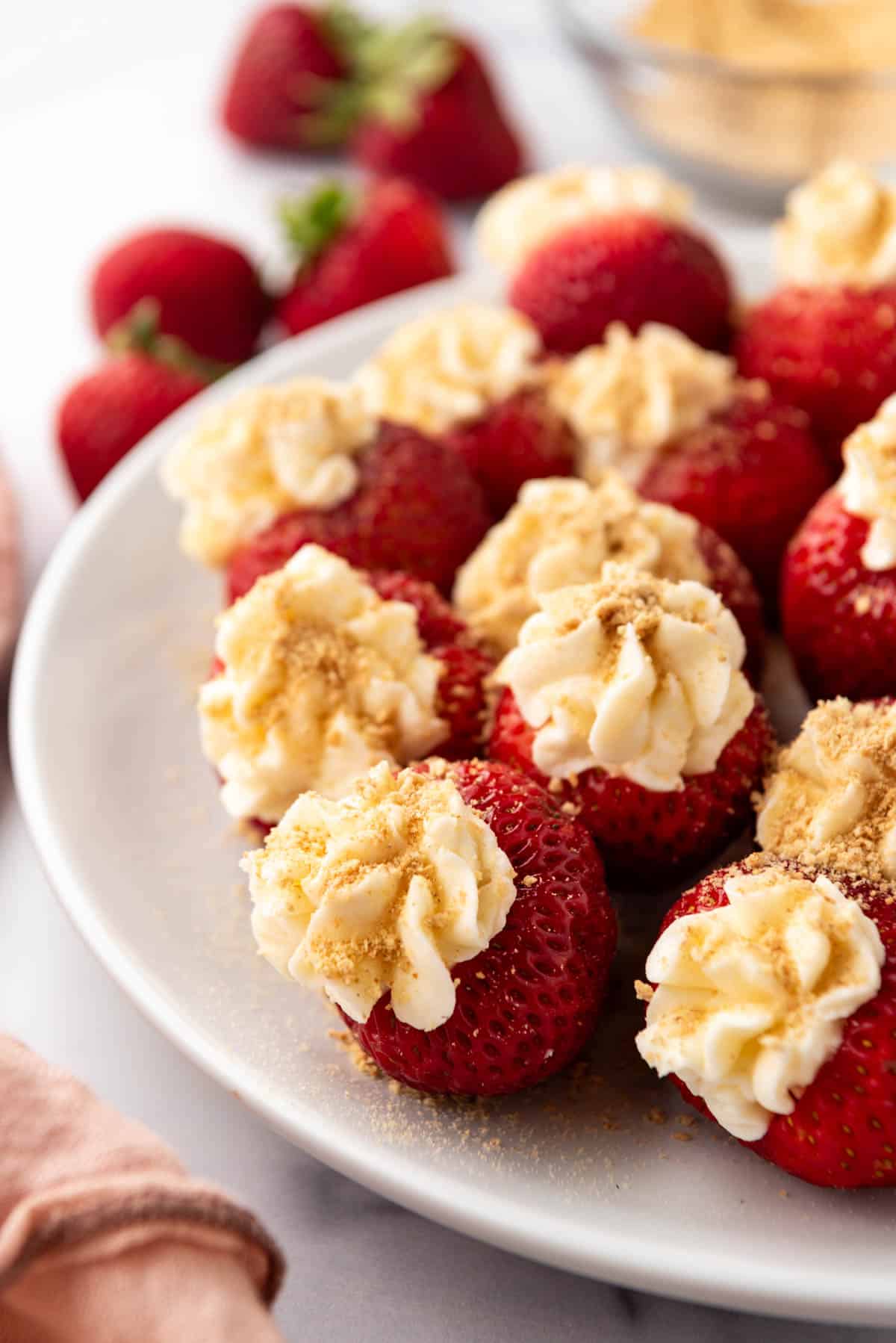 Swirled cheesecake filling in strawberries with crushed graham cracker crumbs on a white plate.