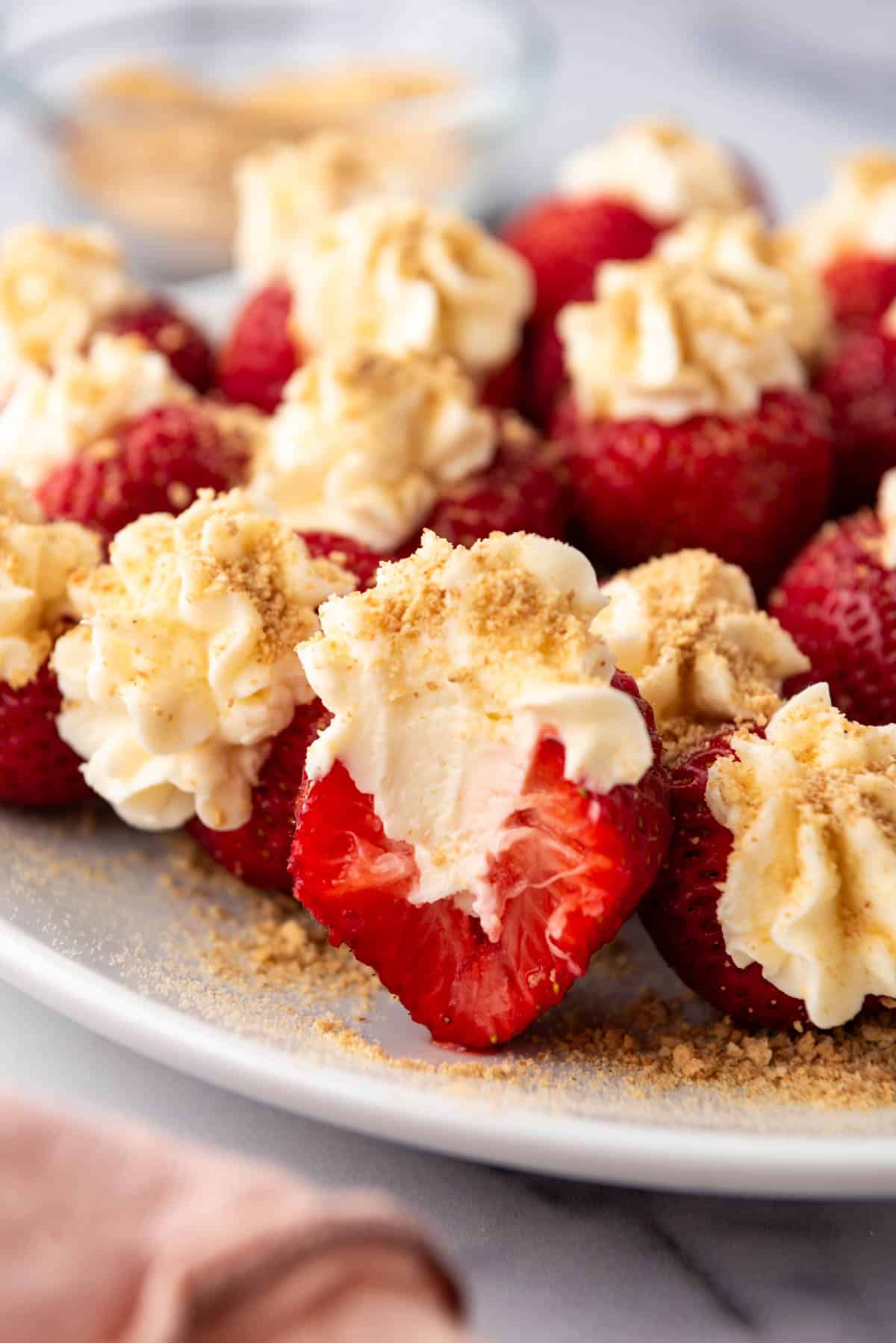 A cheesecake stuffed strawberry that has been bitten in half on a plate with more strawberries.