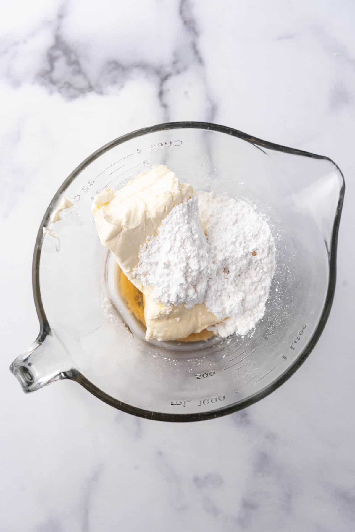 Combining cream cheese, powdered sugar, and vanilla extract in a glass mixing bowl.