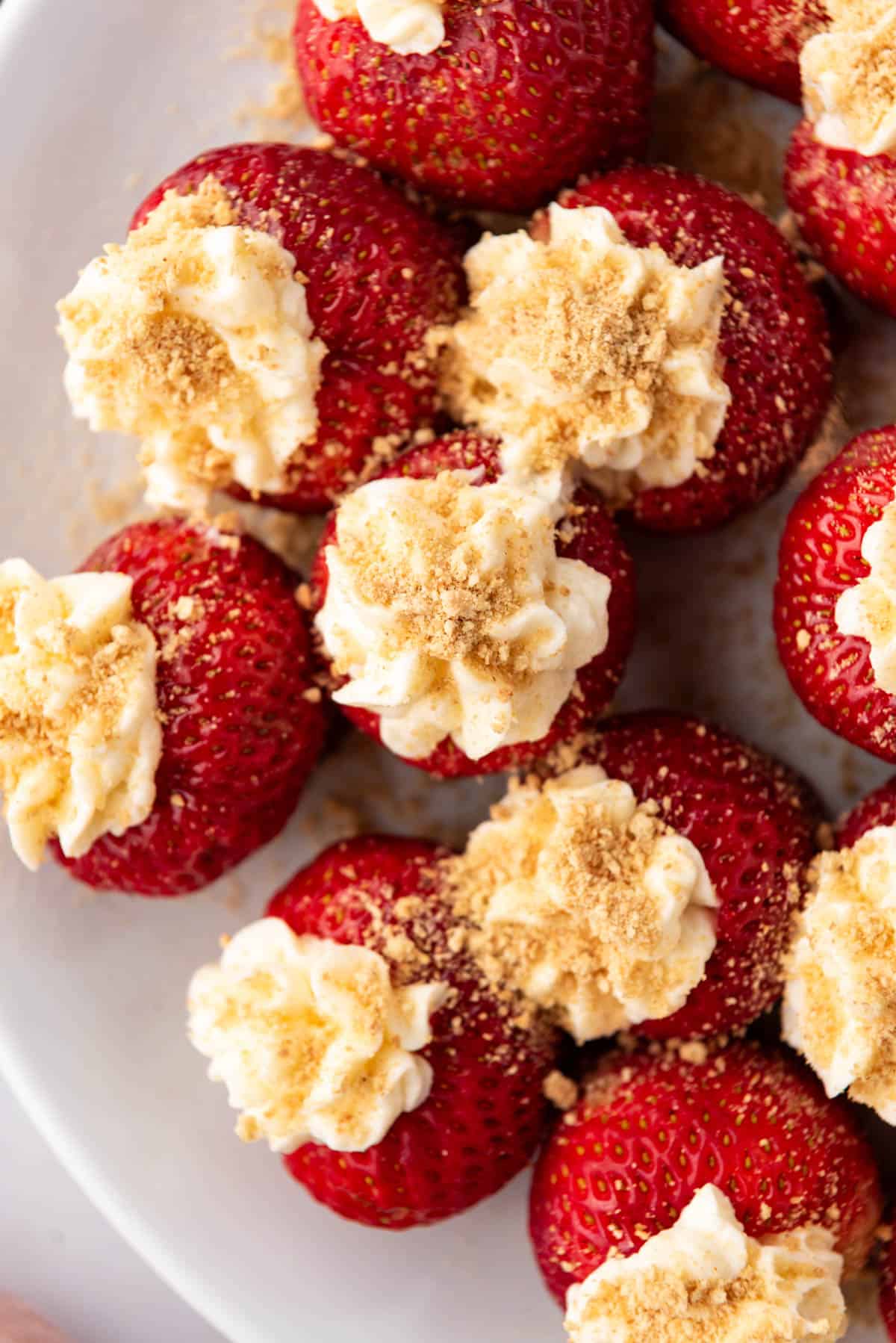 A close up image of strawberries stuffed with no-bake cheesecake filling and sprinkled with graham cracker crumbs.