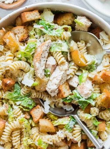 A close up image of pasta salad made with seared chicken breasts, pasta, lettuce, and croutons.