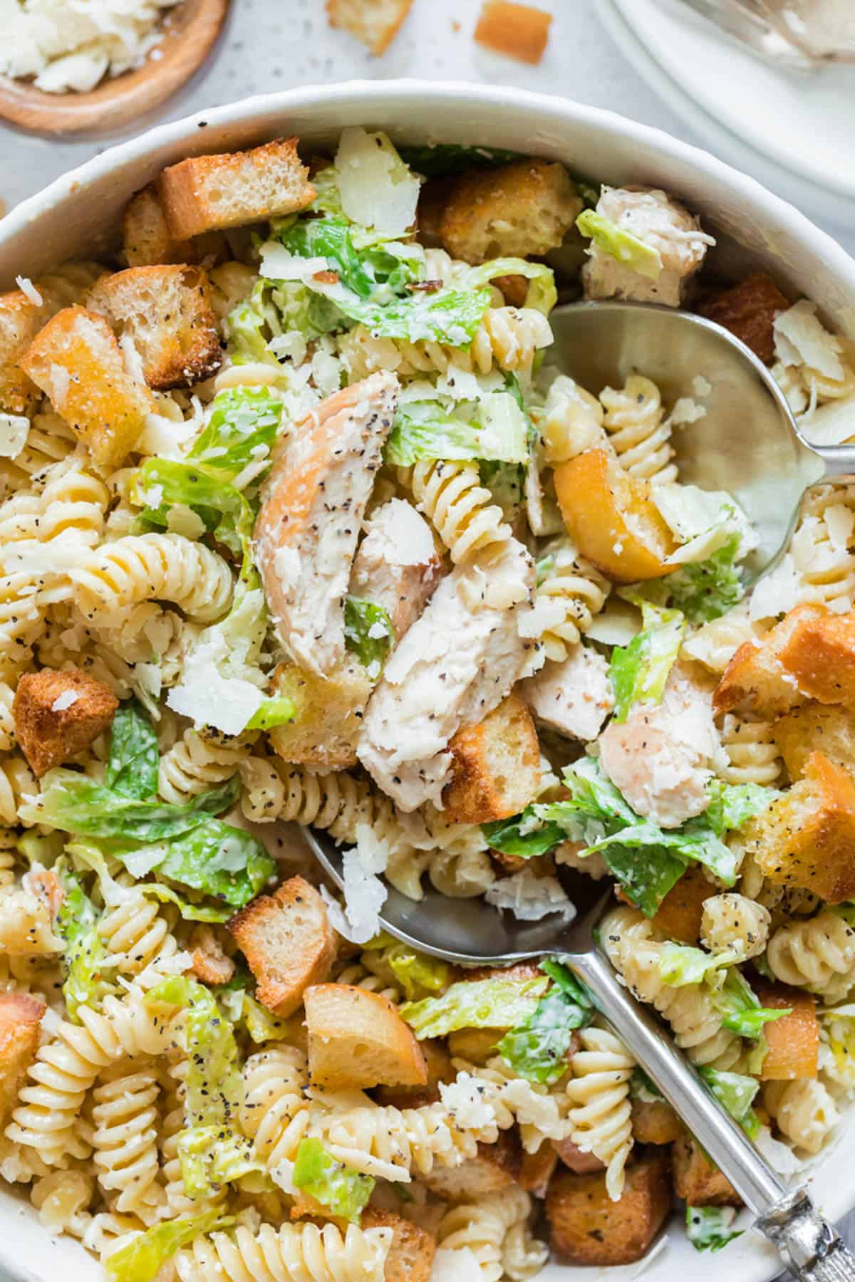 A close up image of pasta salad made with seared chicken breasts, pasta, lettuce, and croutons.