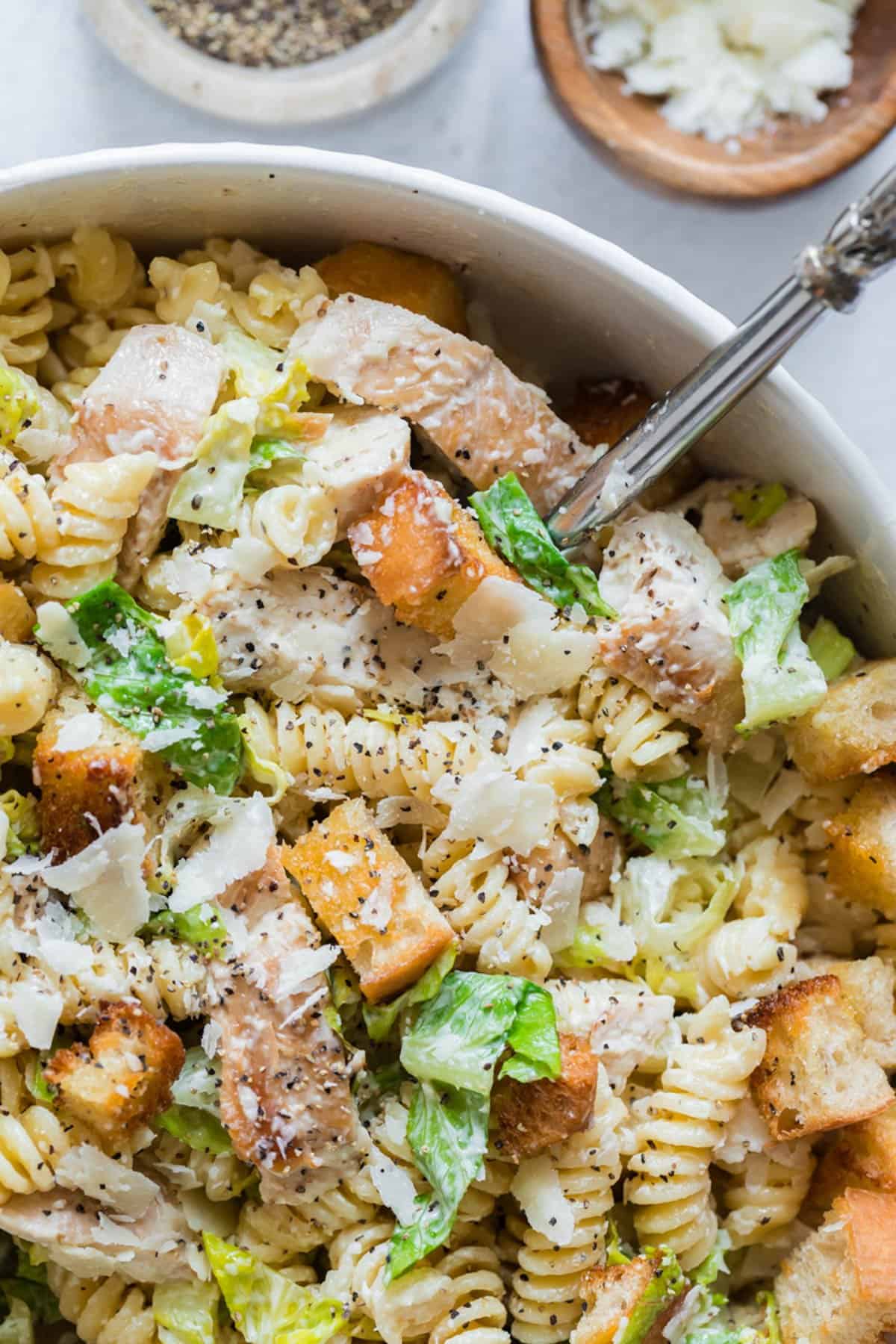 A close up image of a serving spoon lifting a spoonful of chicken caesar pasta salad from a bowl.