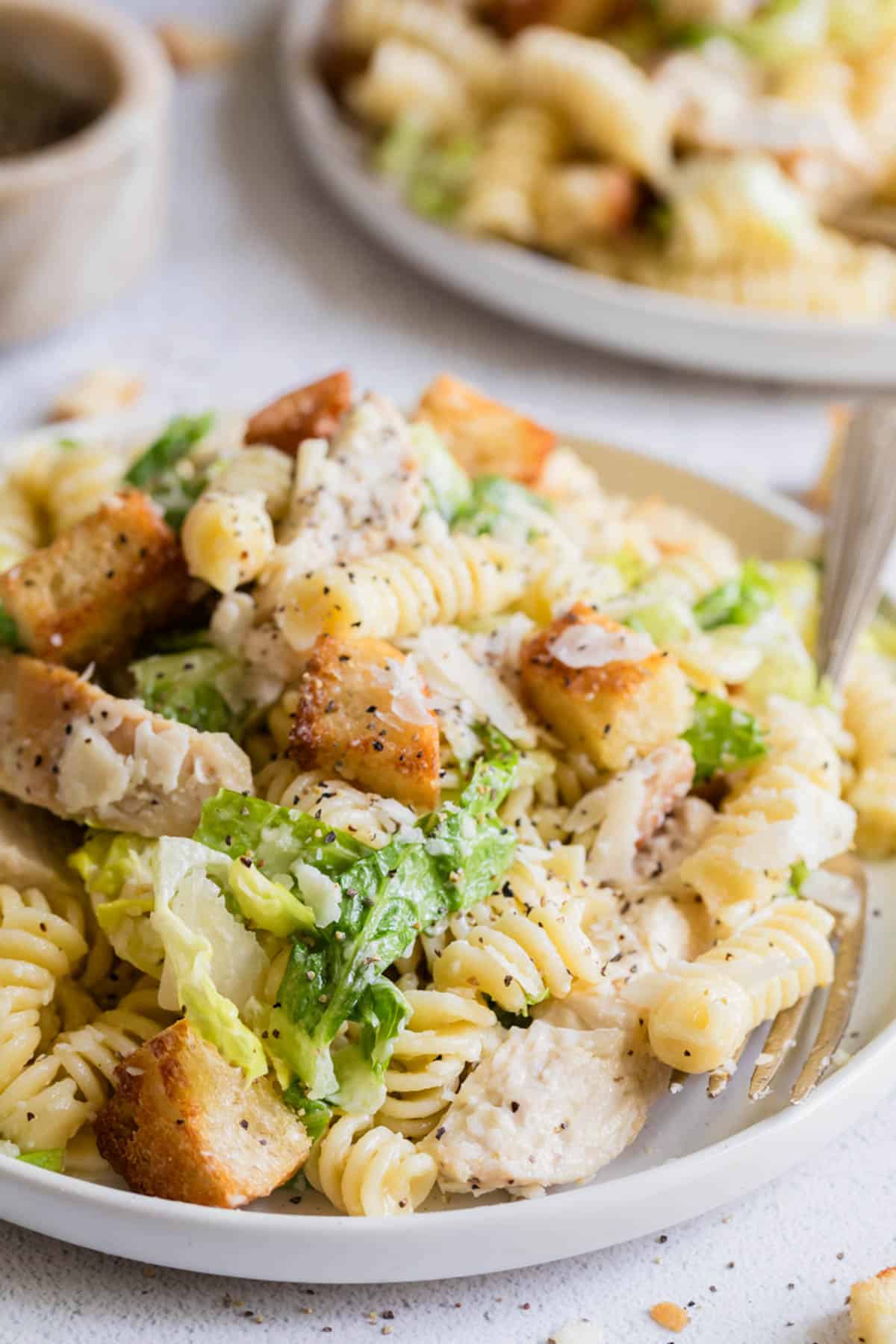 A side view of a plate of chicken caesar pasta salad.