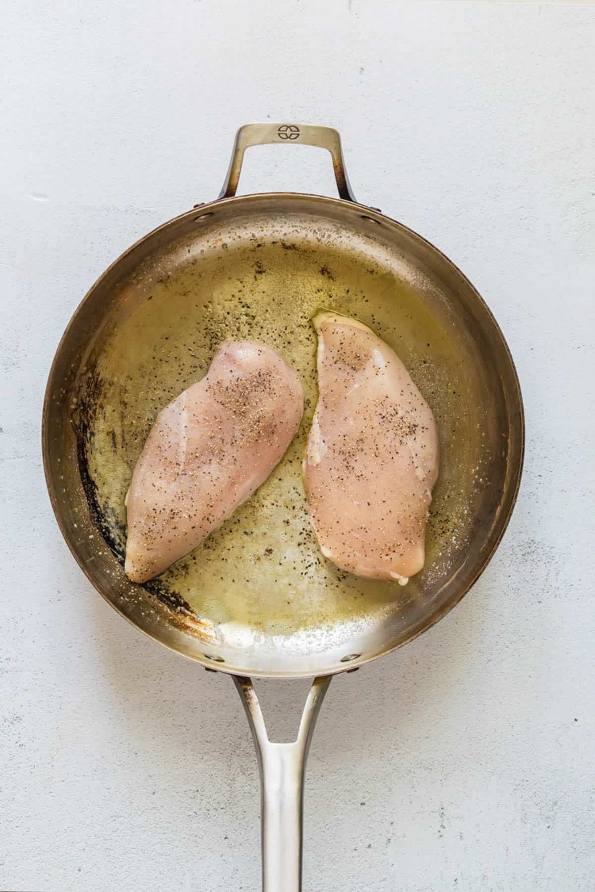 Searing seasoned chicken breasts in a pan.