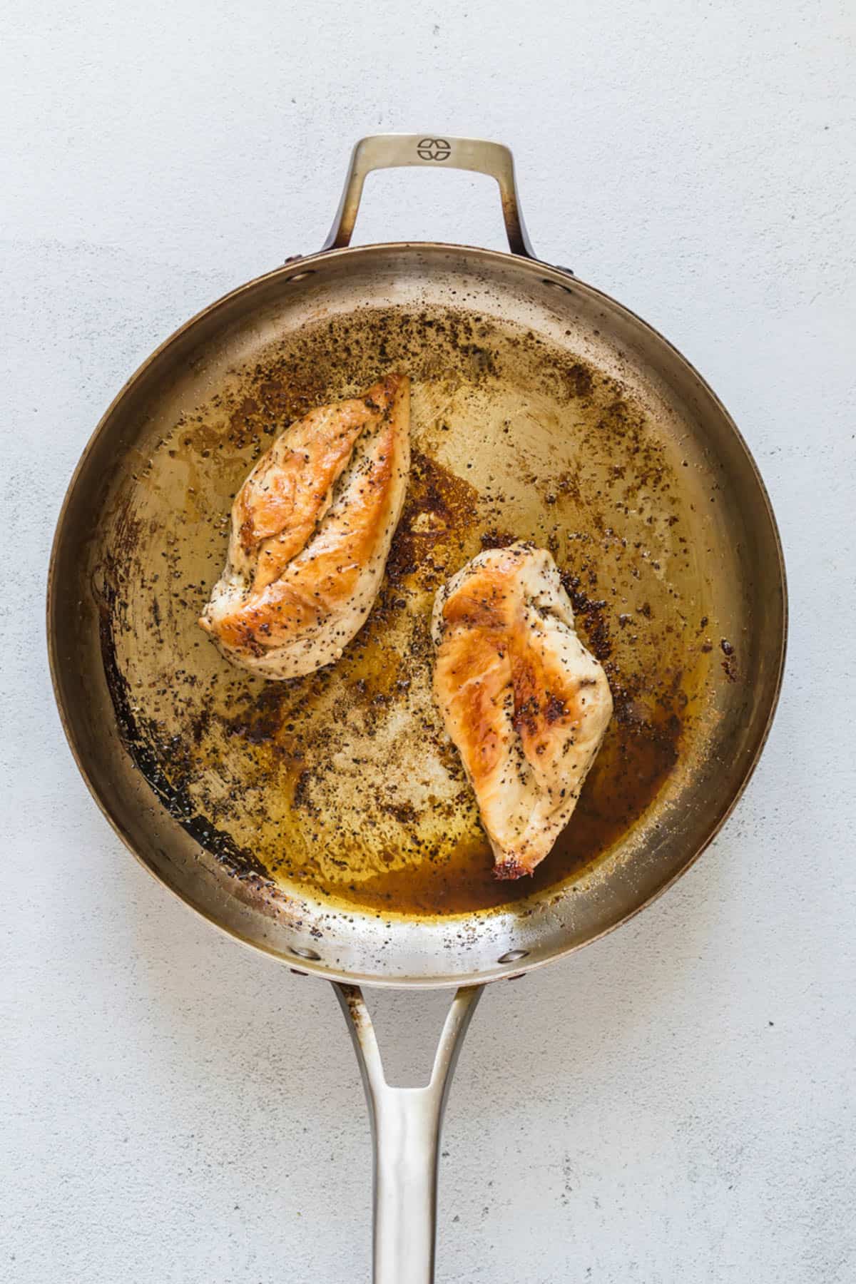 Two pan-seared chicken breasts in the pan.