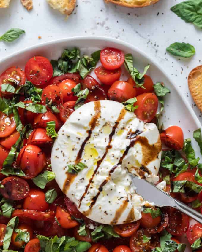 A close image of a ball of burrata cheese on top of tomatoes and basil leaves.