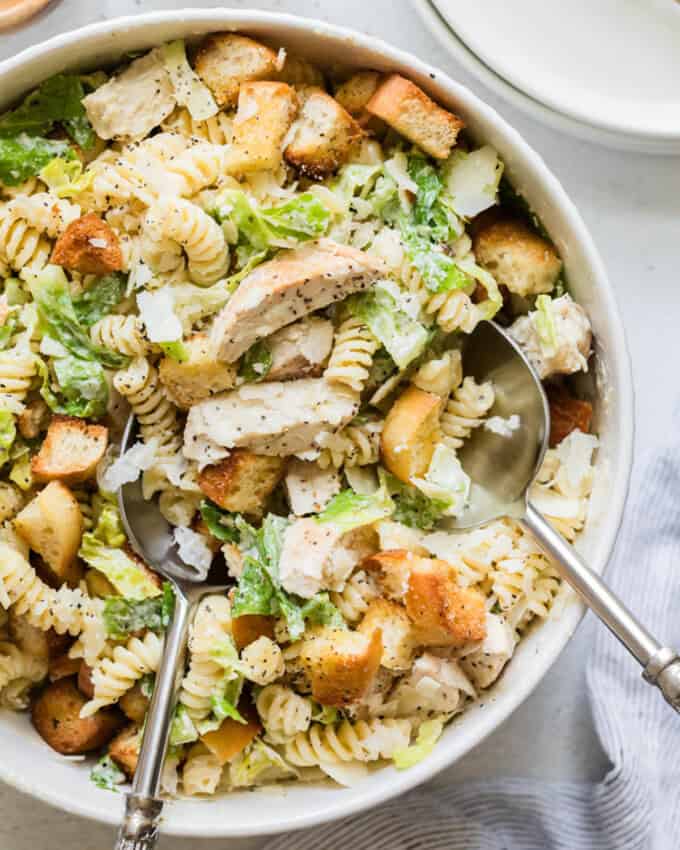 A close up image of a serving spoon lifting a spoonful of chicken caesar pasta salad from a bowl.