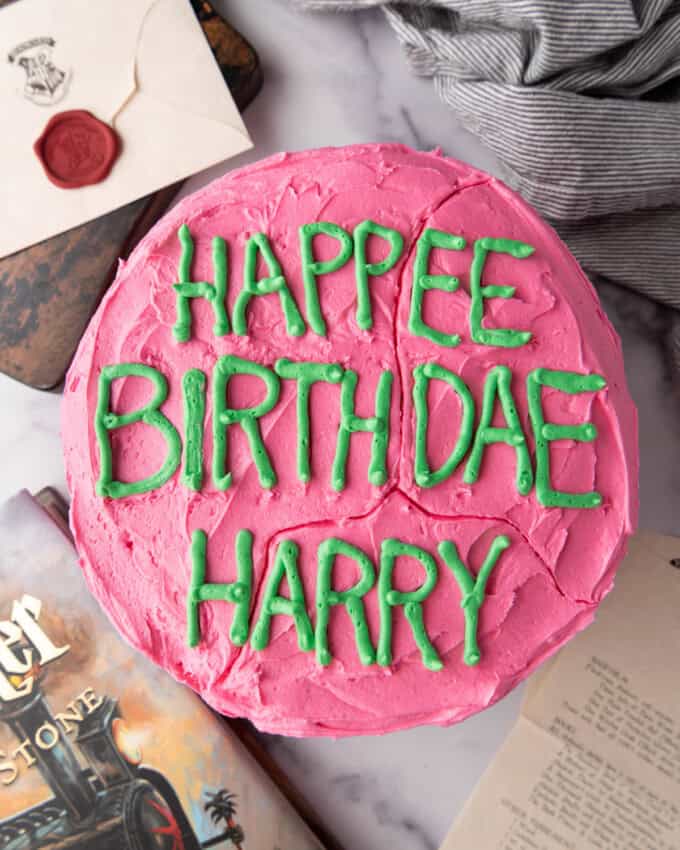 An overhead image of a Harry Potter birthday cake next to green frosting in a piping bag and an illustrated Harry Potter and the Philosopher's Stone book.