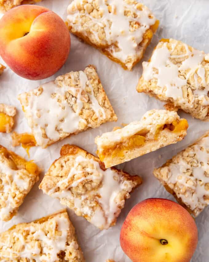 Peach crumb bars with one turned on its side and fresh peaches nearby.