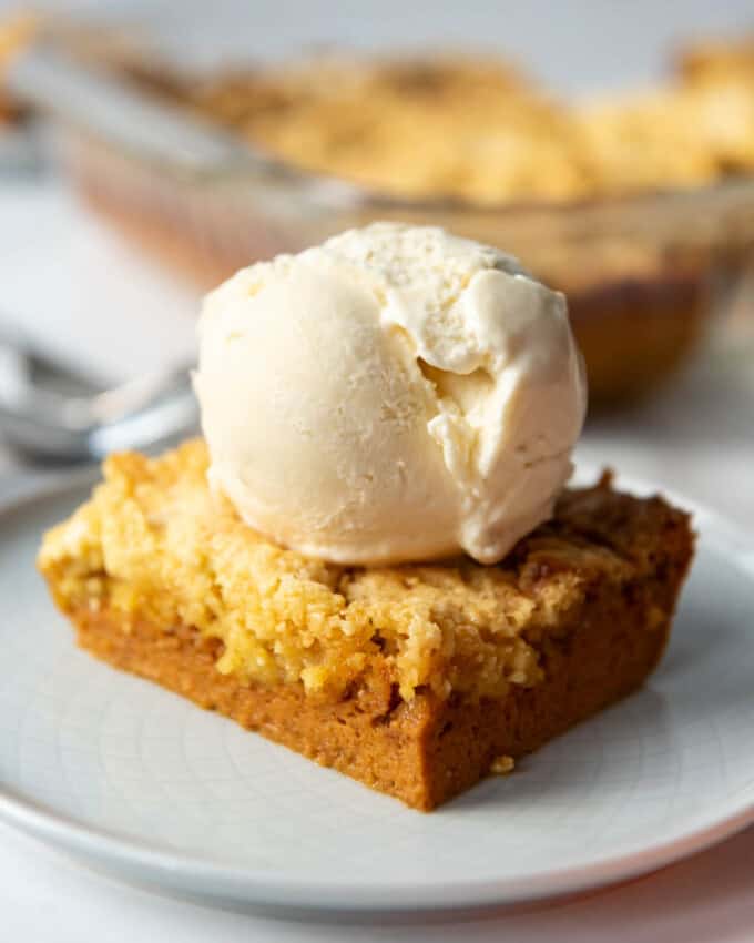 Pumpkin dump cake with vanilla ice cream on top on a white plate.