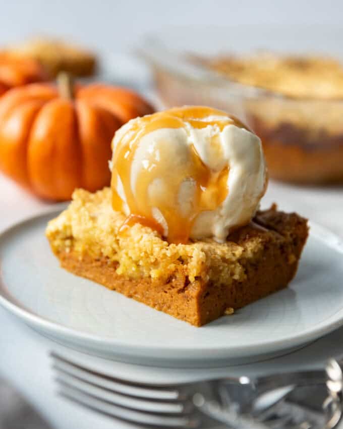 An image of a piece of pumpkin dump cake with a scoop of vanilla ice cream and caramel sauce on top.