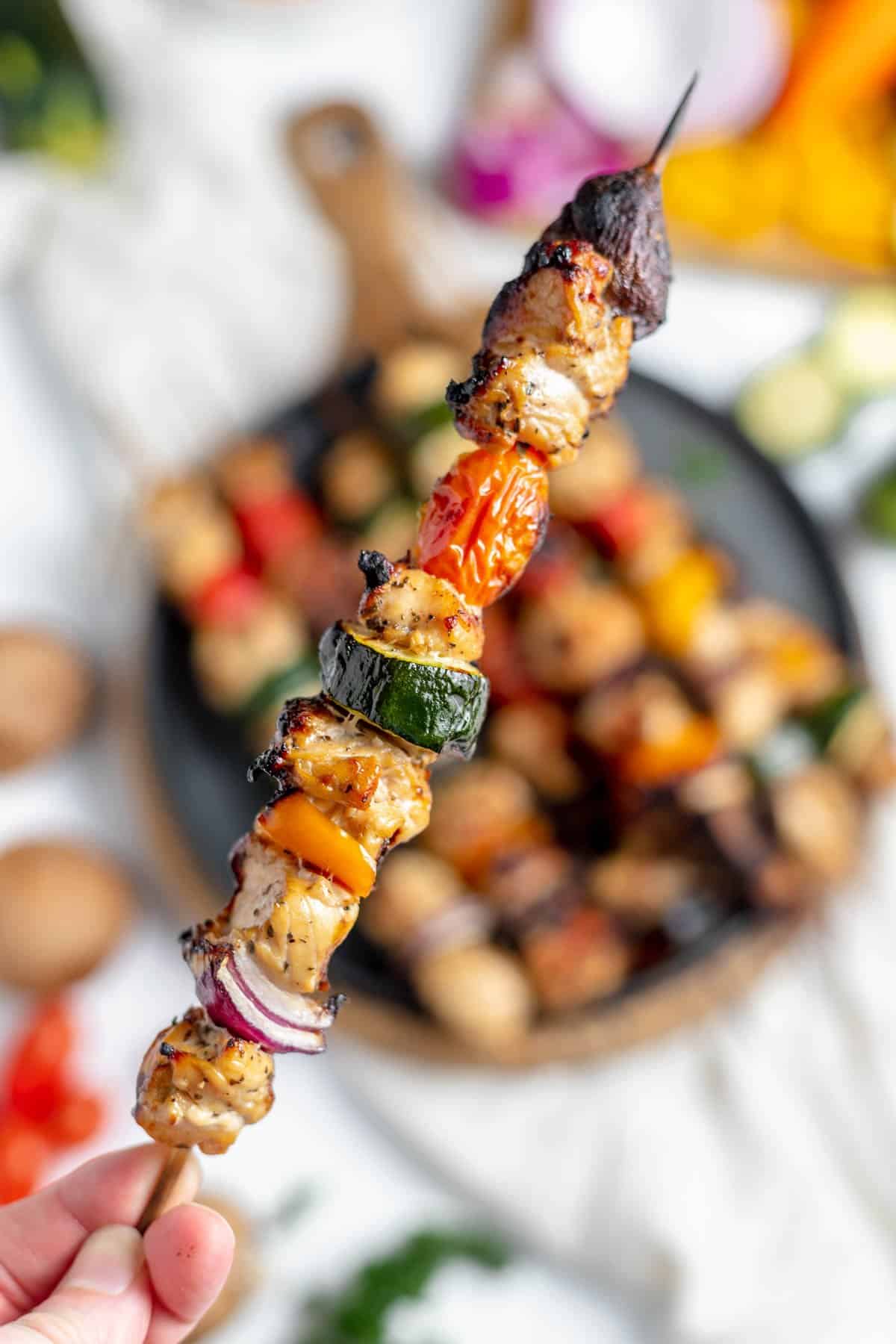 A hand holding a grilled chicken kabob skewer.