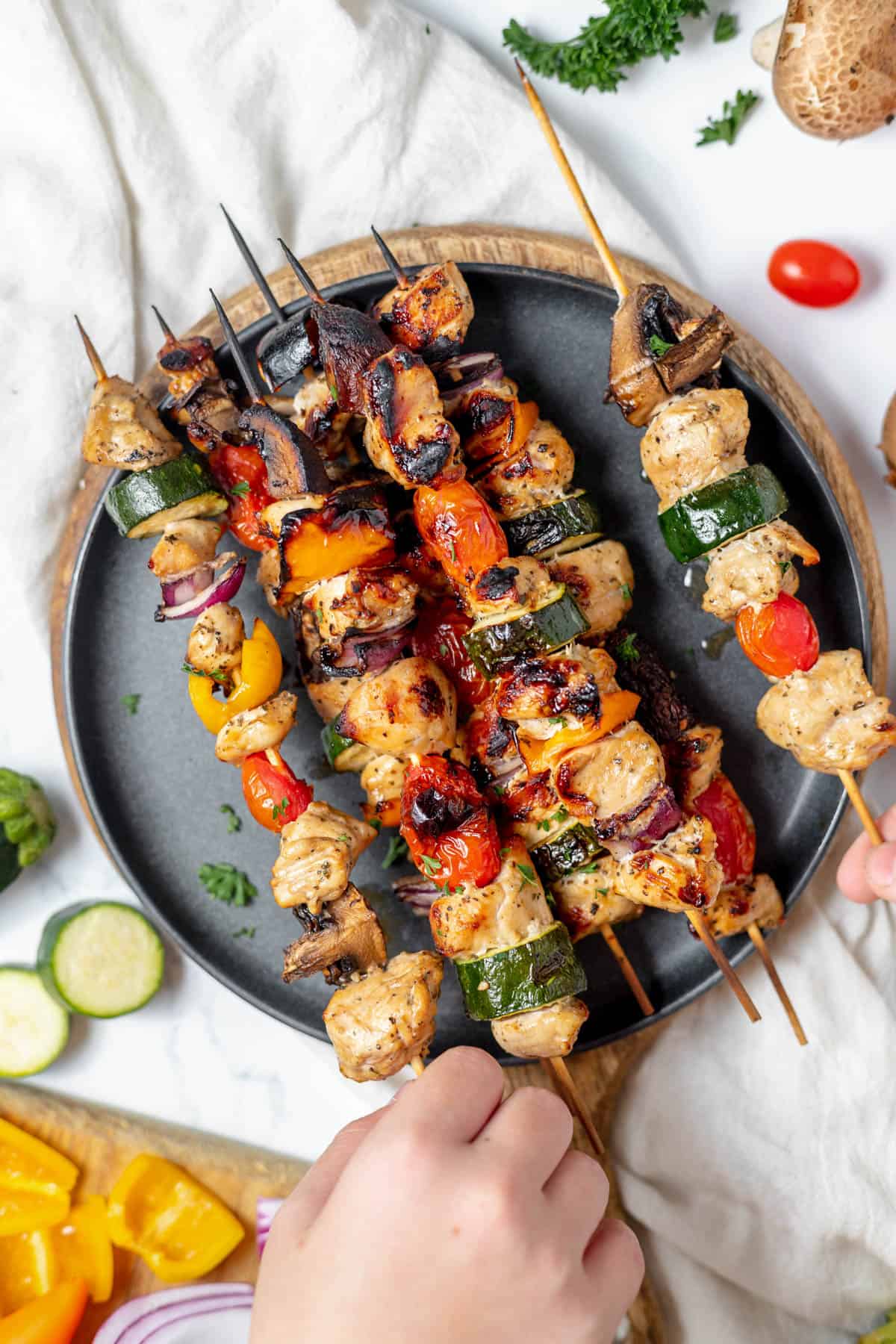 A hand reaching for a grilled chicken kabob.