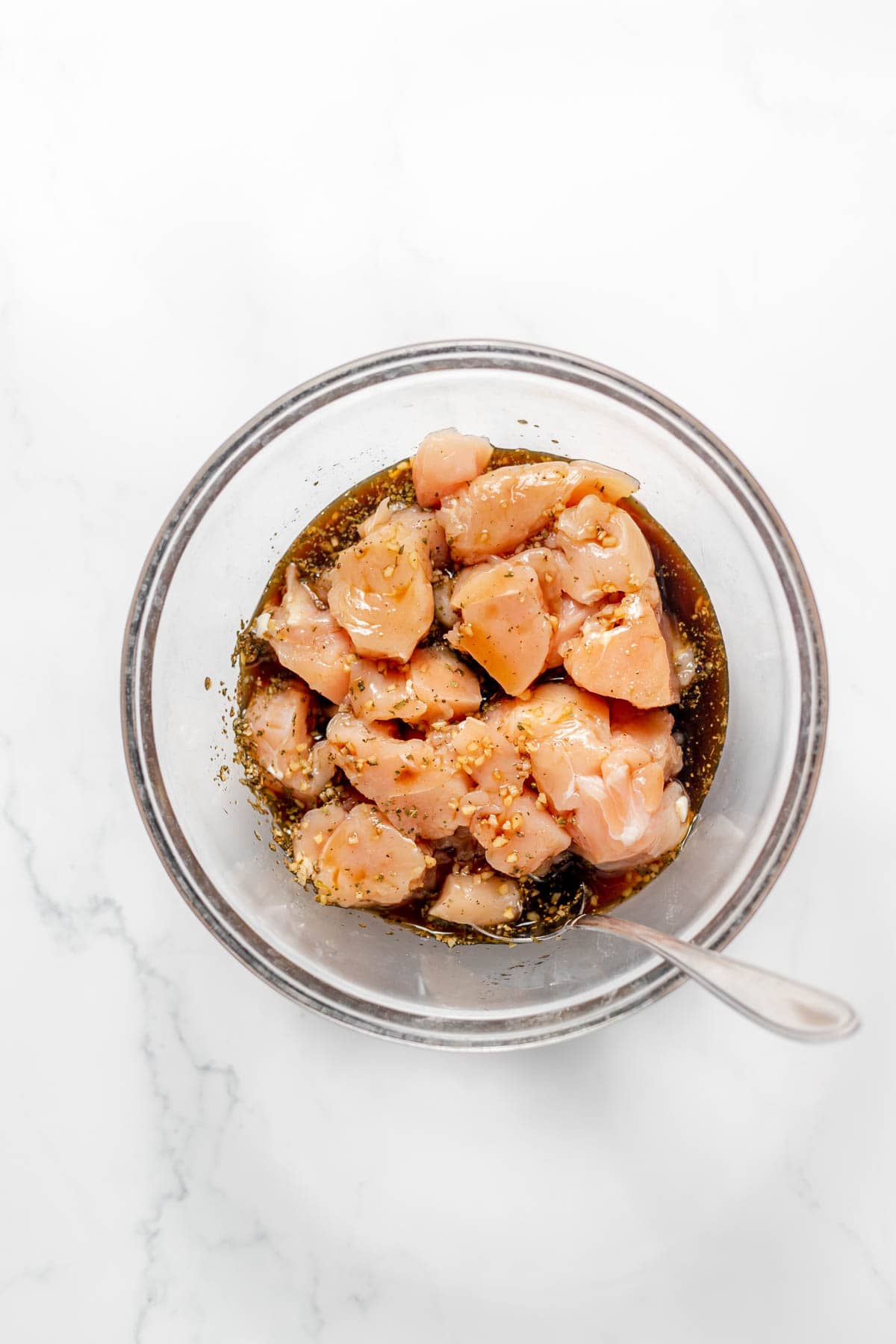 Marinating bite-size chunks of chicken breast in a marinade in a glass bowl.