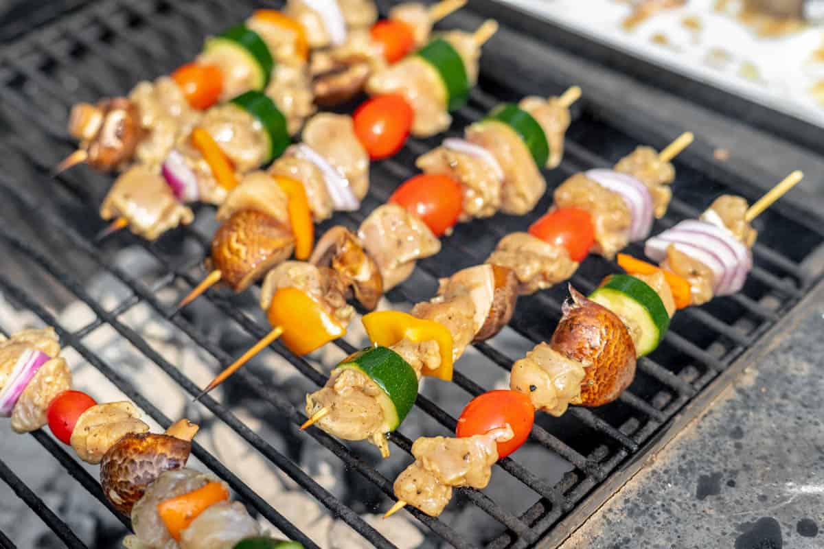 Chicken and vegetable skewers on a grill over hot coals.