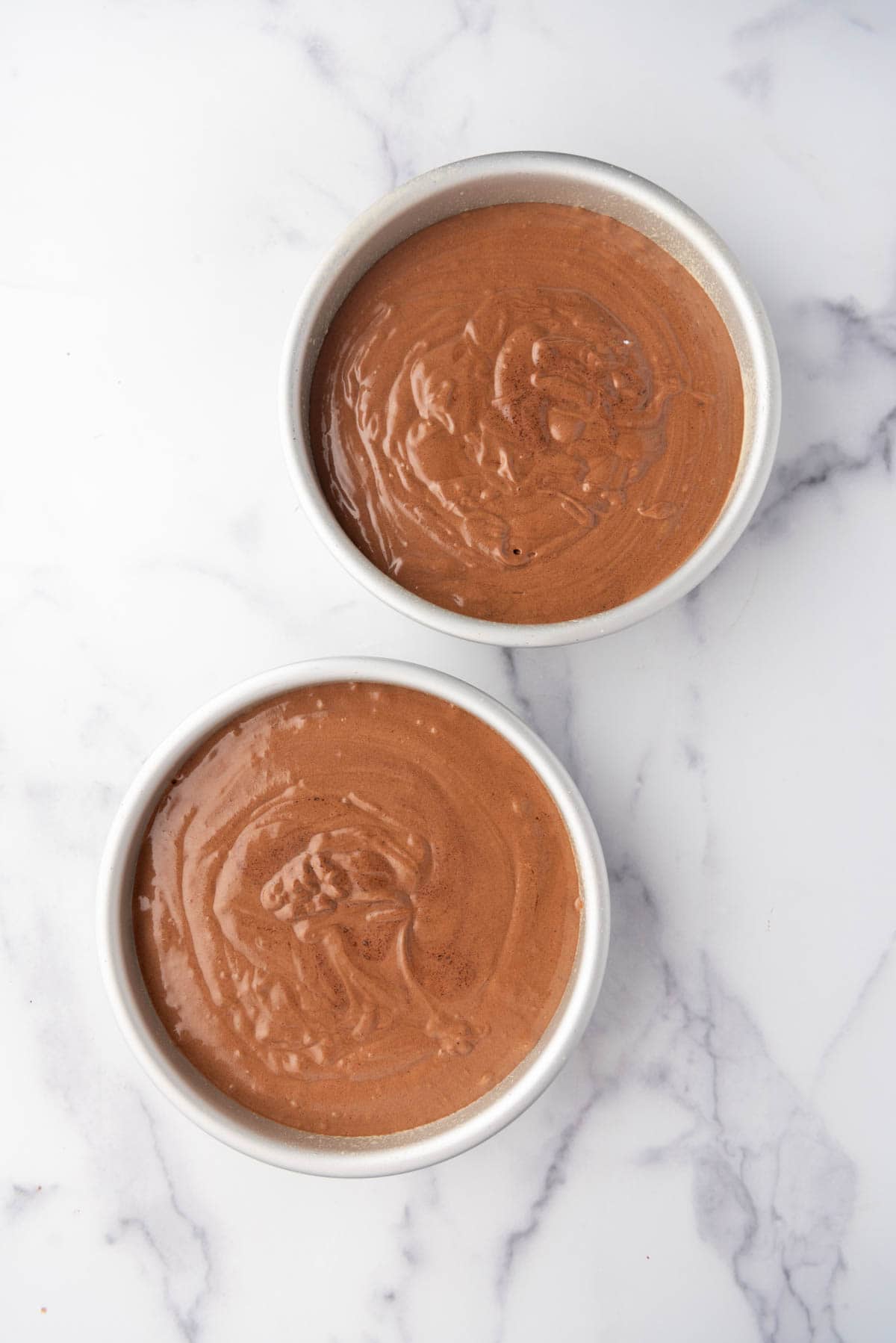 Dividing chocolate cake batter evenly between two round cake pans.