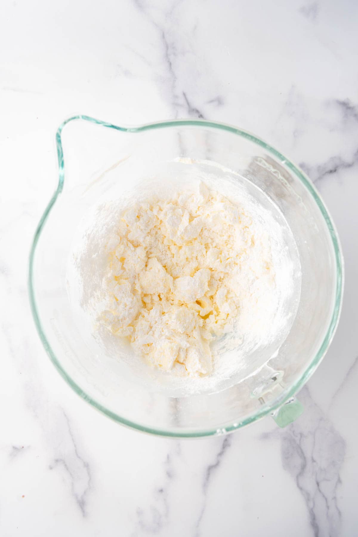 Combining powdered sugar and butter in a large glass mixing bowl.