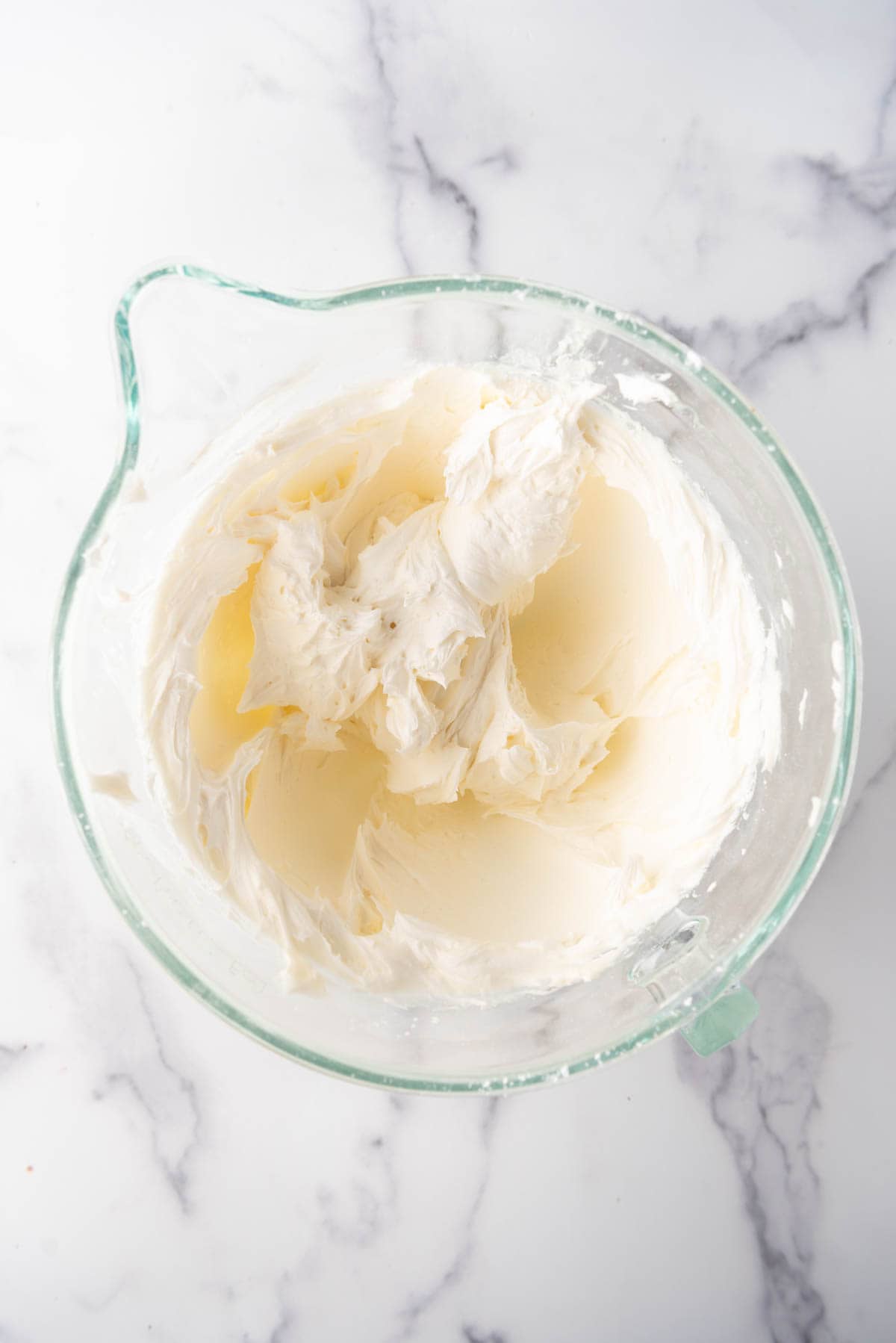 Creamy buttercream frosting in a glass mixing bowl.