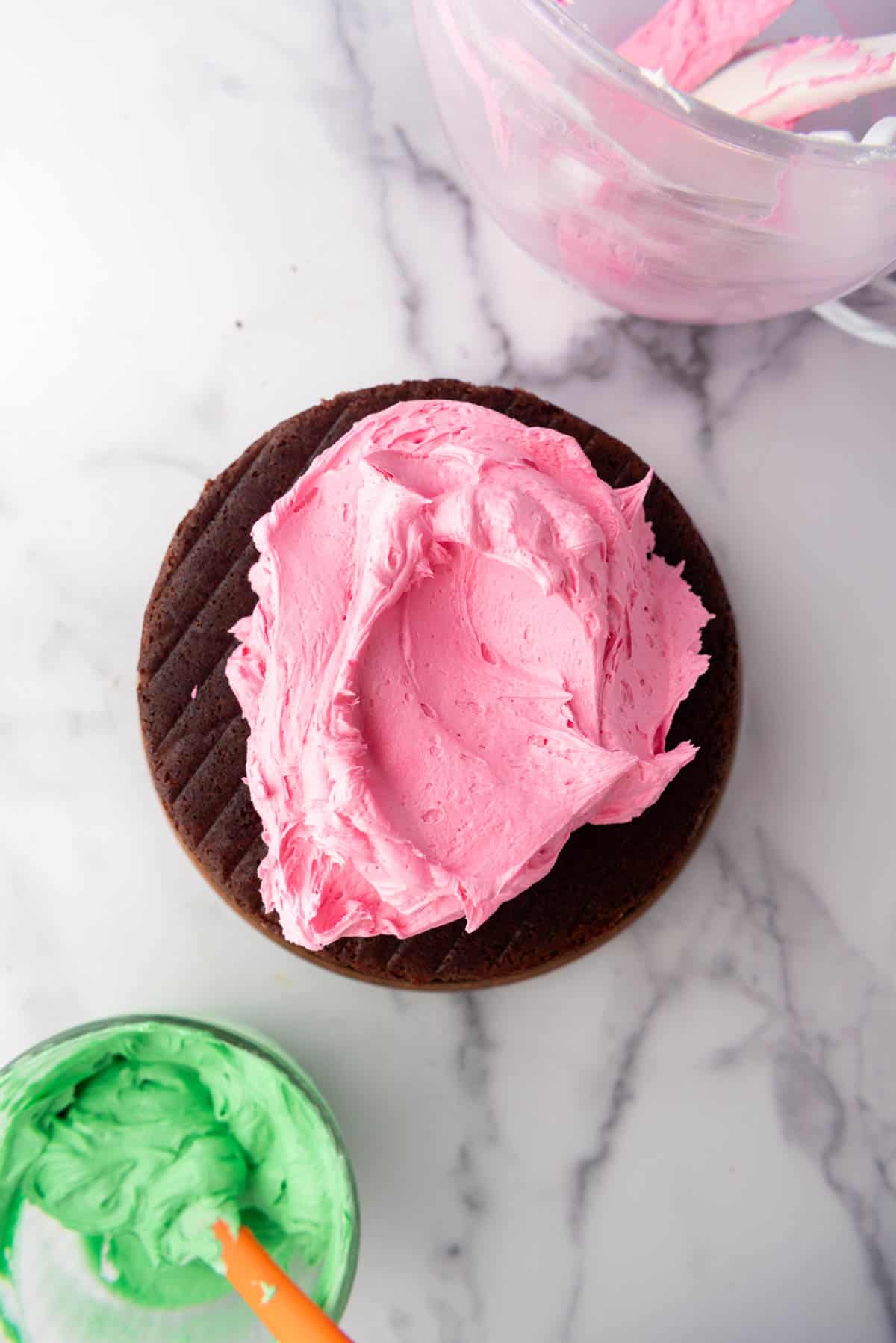 Adding pink frosting to layers of chocolate cake.