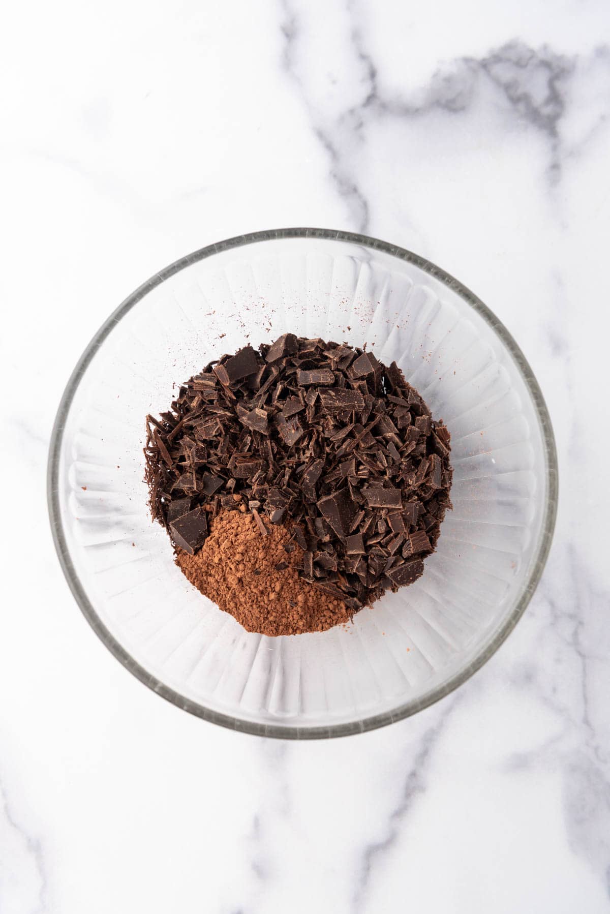 Chopped chocolate and cocoa powder in a glass mixing bowl.