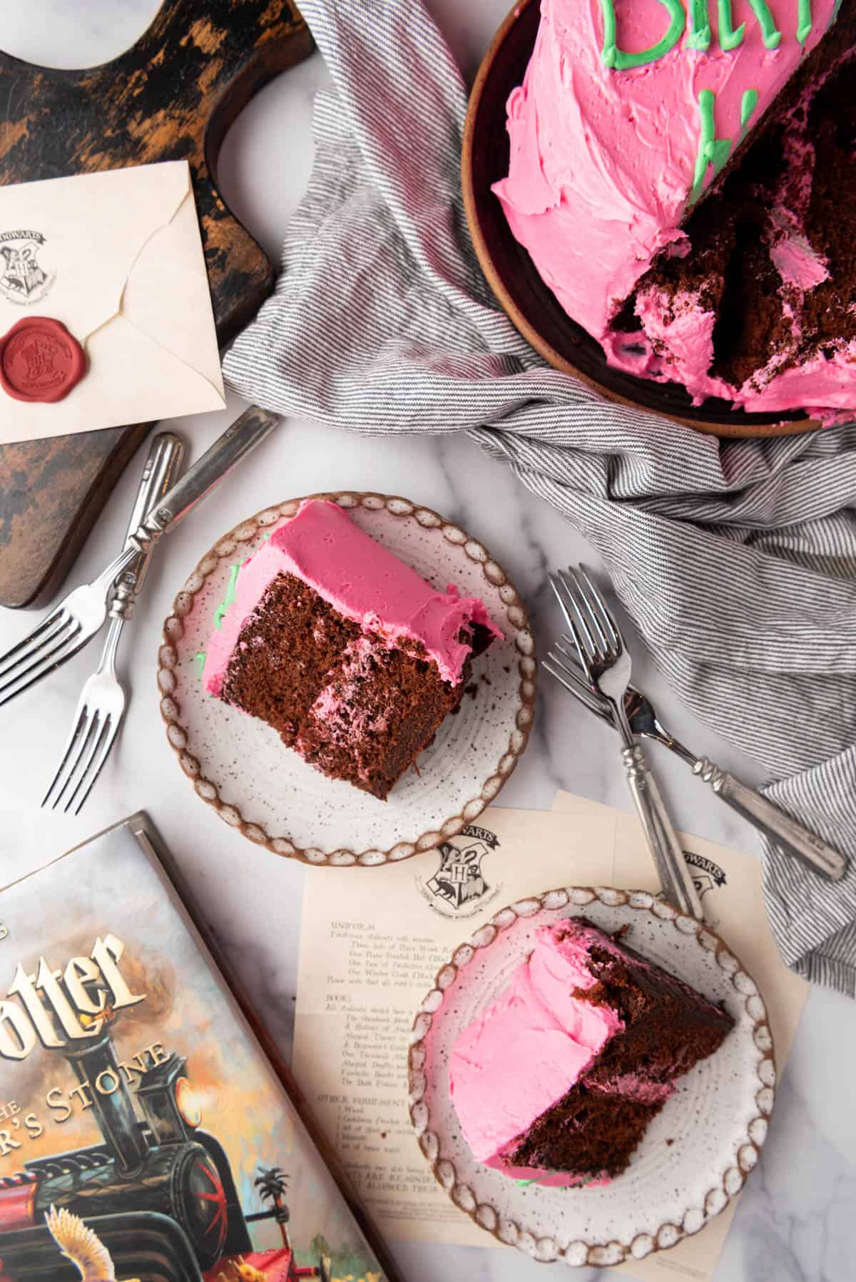 An image of slices of sticky chocolate cake with pink and green frosting on plates.