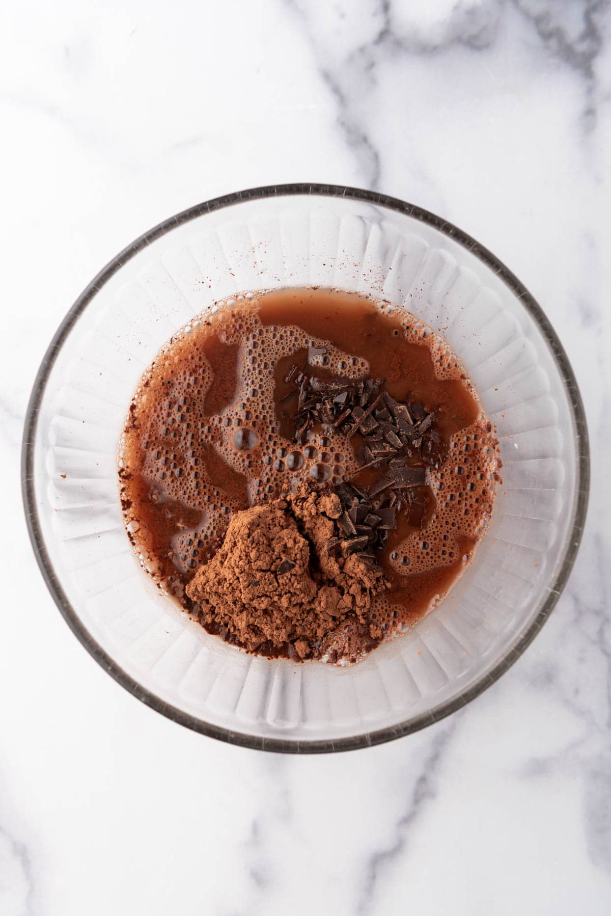 A glass mixing bowl with hot water, chopped semisweet chocolate, and cocoa powder.