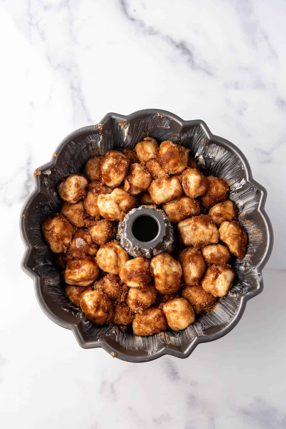 Balls of monkey bread dough in a bundt pan covered in cinnamon sugar and melted butter.