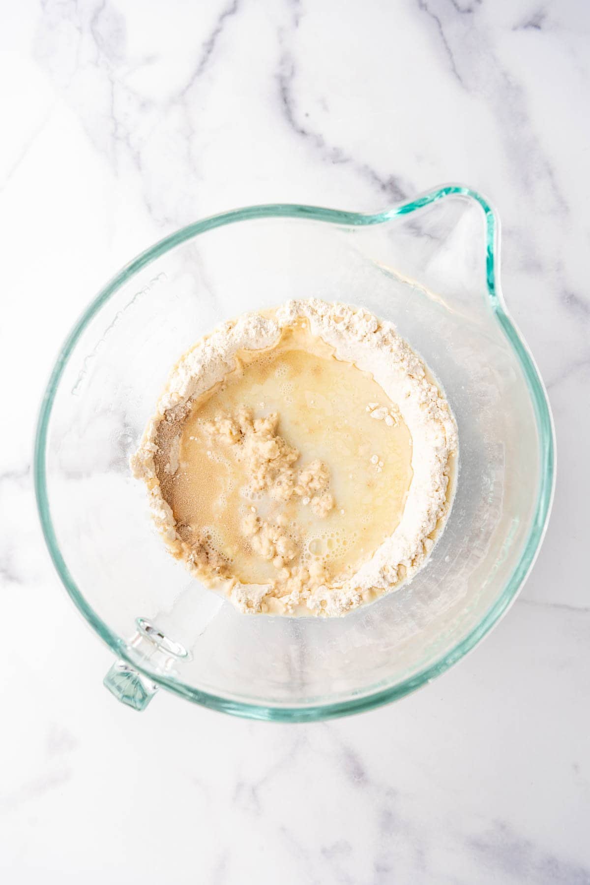 Adding warm liquid to flour and yeast in a mixing bowl.